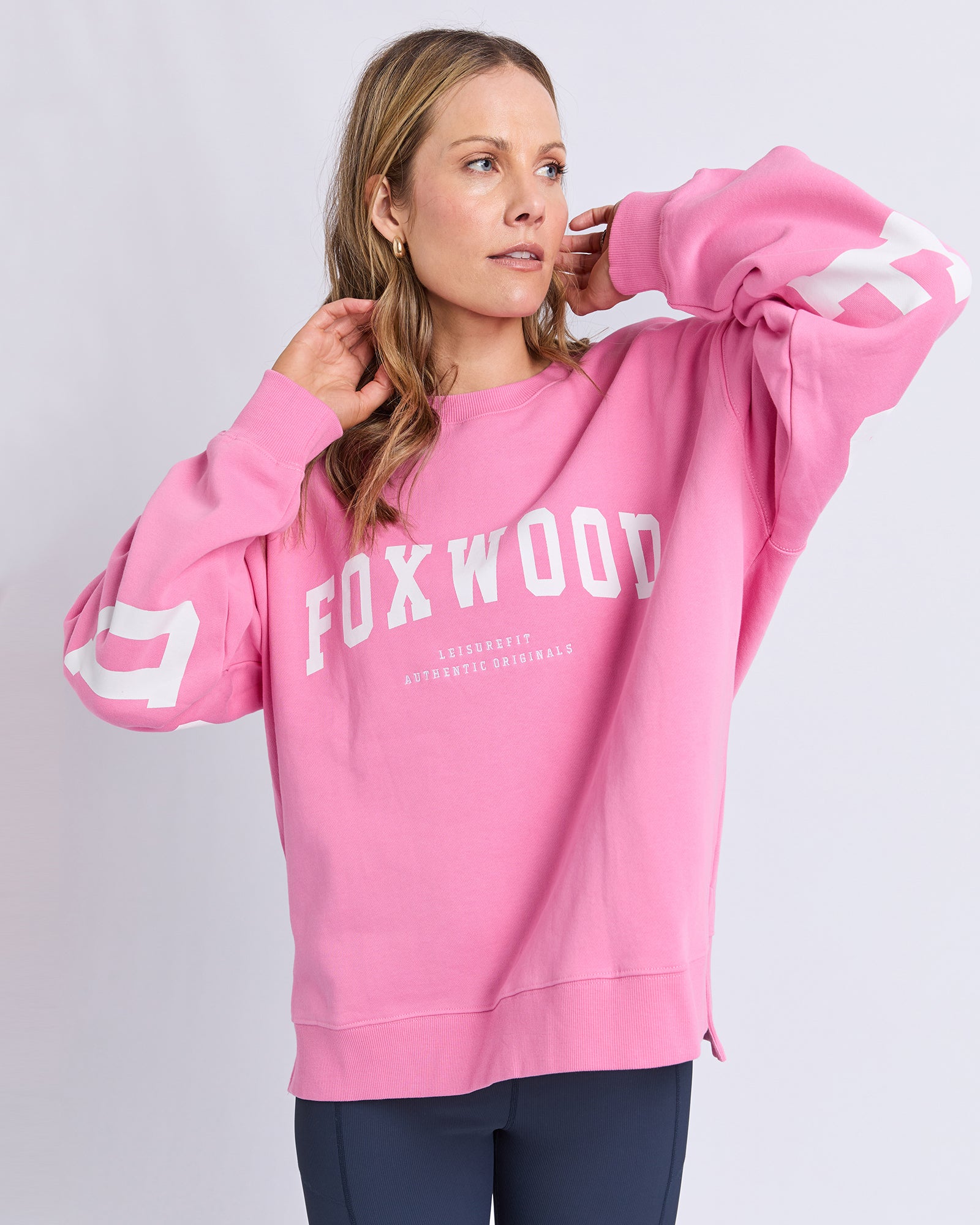 Image of Woman wearing a pink sweatshirt with 'FOXWOOD' branding on a light gray background
