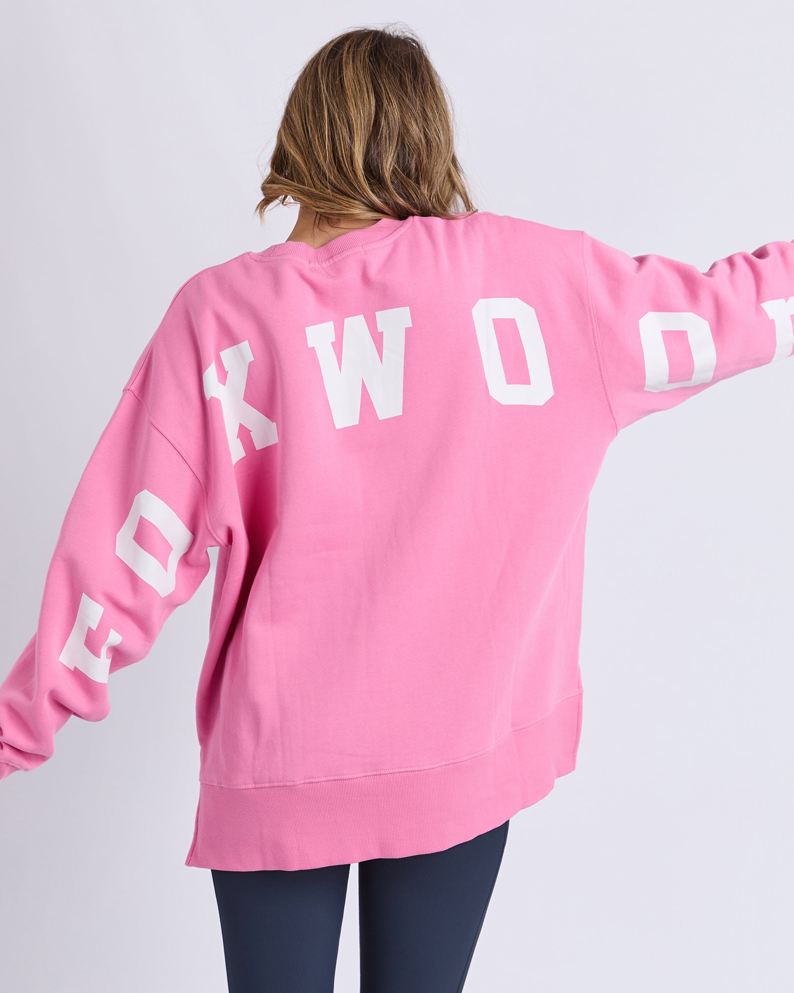 Image of Woman wearing a Foxwood pink sweatshirt with 'FOXWOOD' printed on the back against a white background