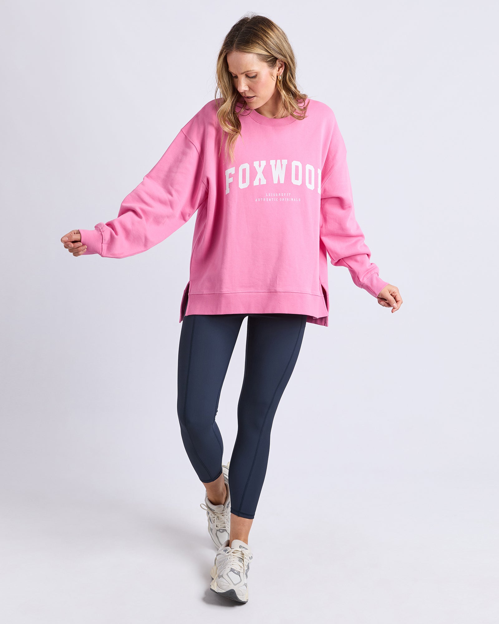Image of Woman wearing a Foxwood pink 'FOXWOOD' sweatshirt and navy leggings on a light purple background
