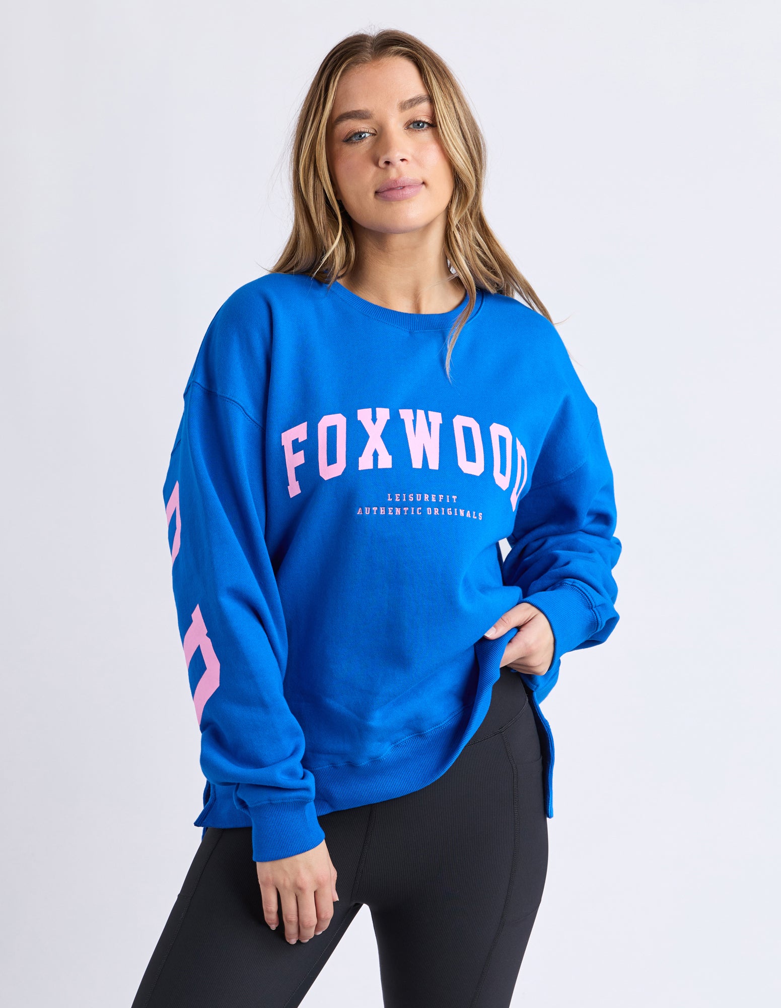 Woman wearing a Foxwood blue jumper with 'FOXWOOD' printed on it in  pink against a white background