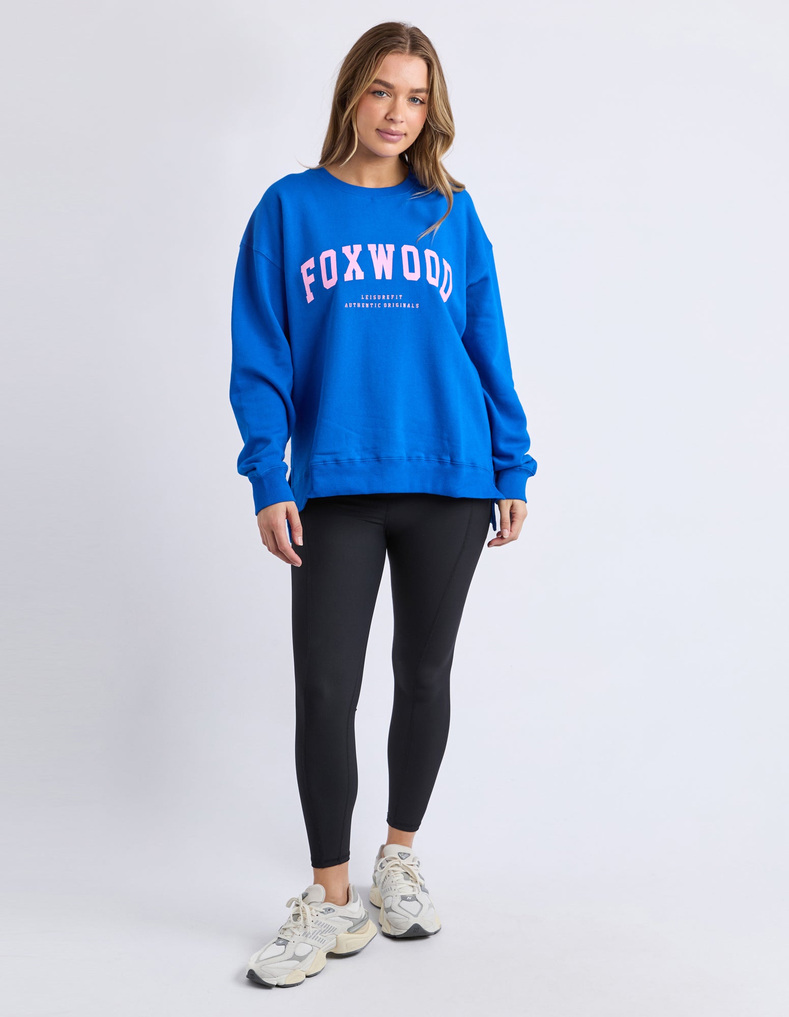 Image of Woman wearing a blue 'FOXWOOD' jumper with pink print on a white background
