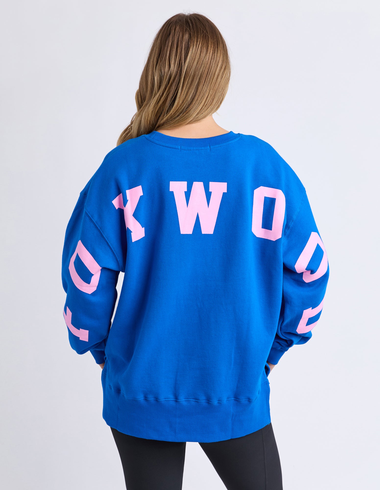 Image of Woman wearing a blue Foxwood Jumper with pink text on a white background