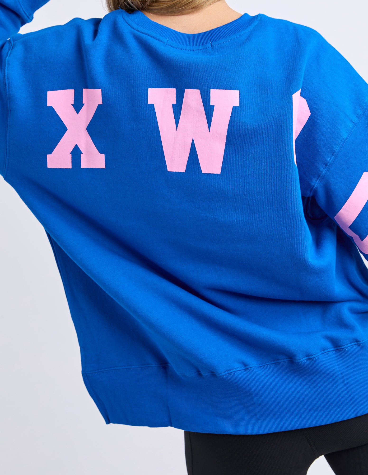 Image of Woman wearing a Foxwood Blue jumper with pink letters showing back view on a white background