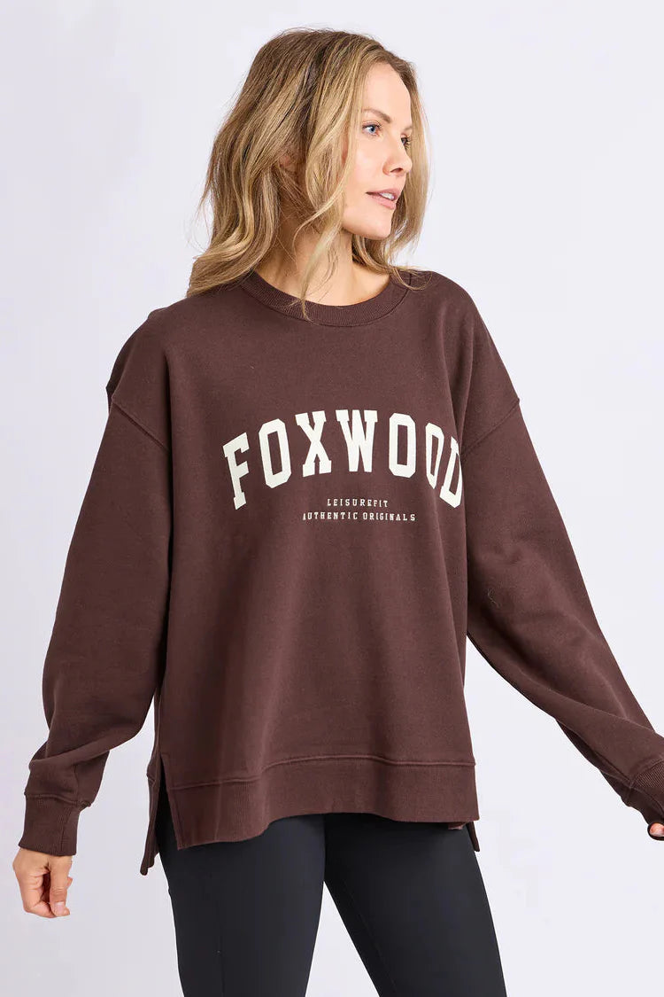 Woman wearing a brown sweatshirt with 'FOXWOOD' printed on it against a white background