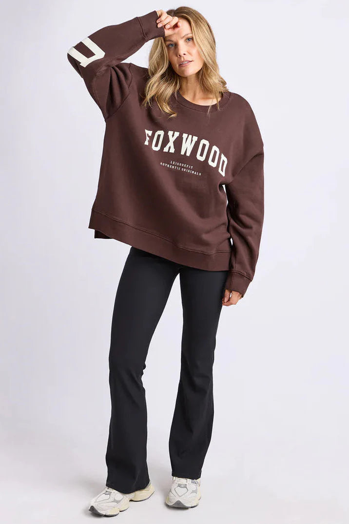 Image of Woman wearing a brown sweatshirt with 'FOXWOOD' printed on it against a white background