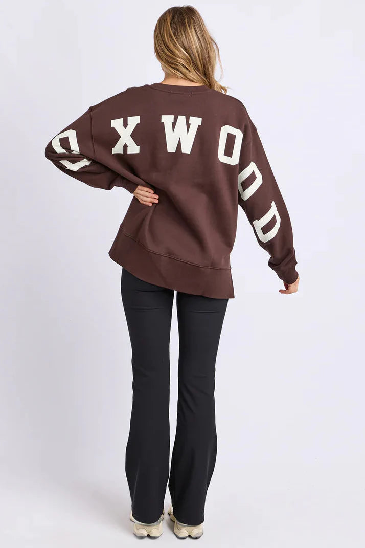 Person wearing a brown sweatshirt with 'FOXWOOD' printed on the back against a white background