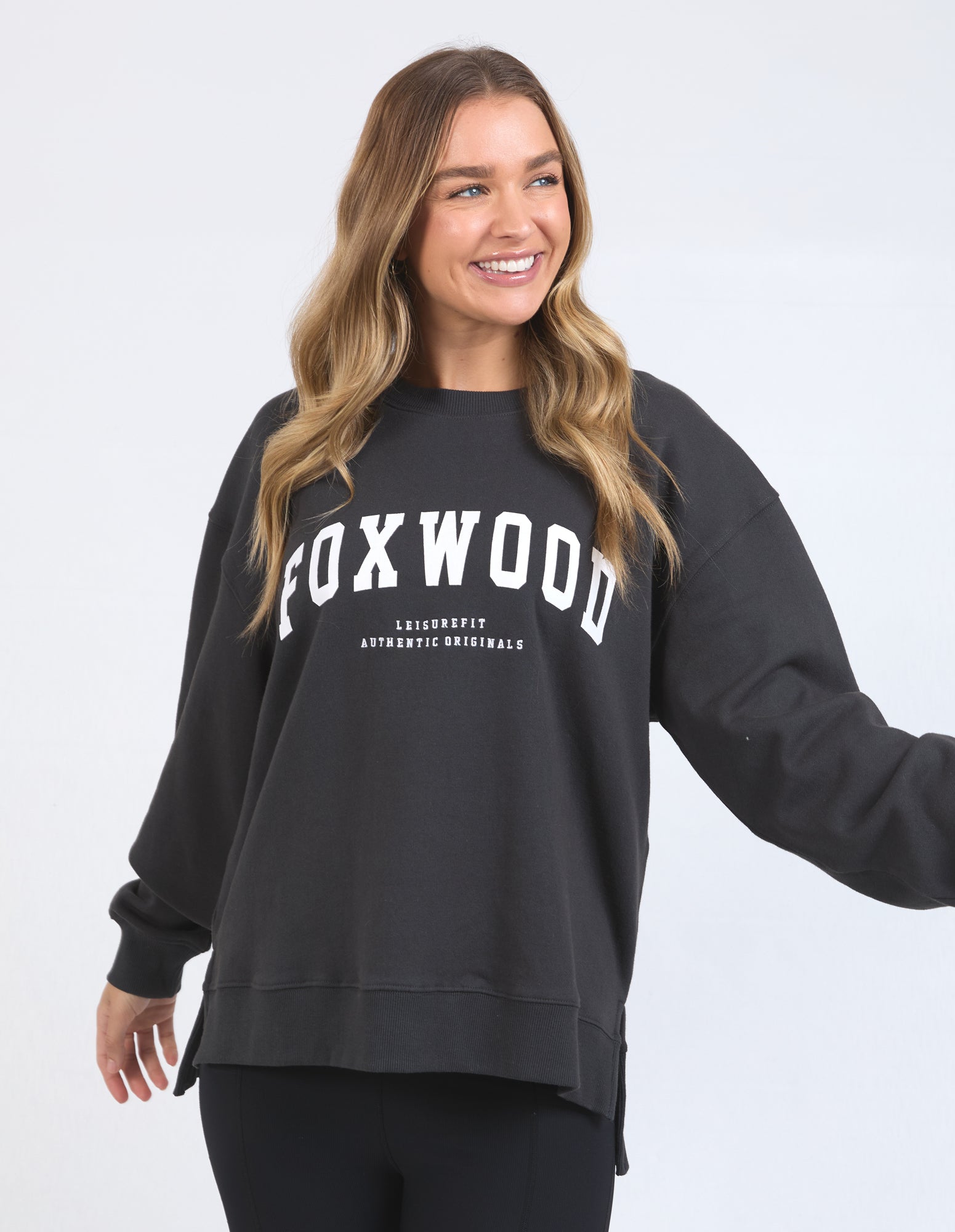 A woman smiling and wearing a dark grey Foxwood sweatshirt with a relaxed fit and text print on the front chest and back.