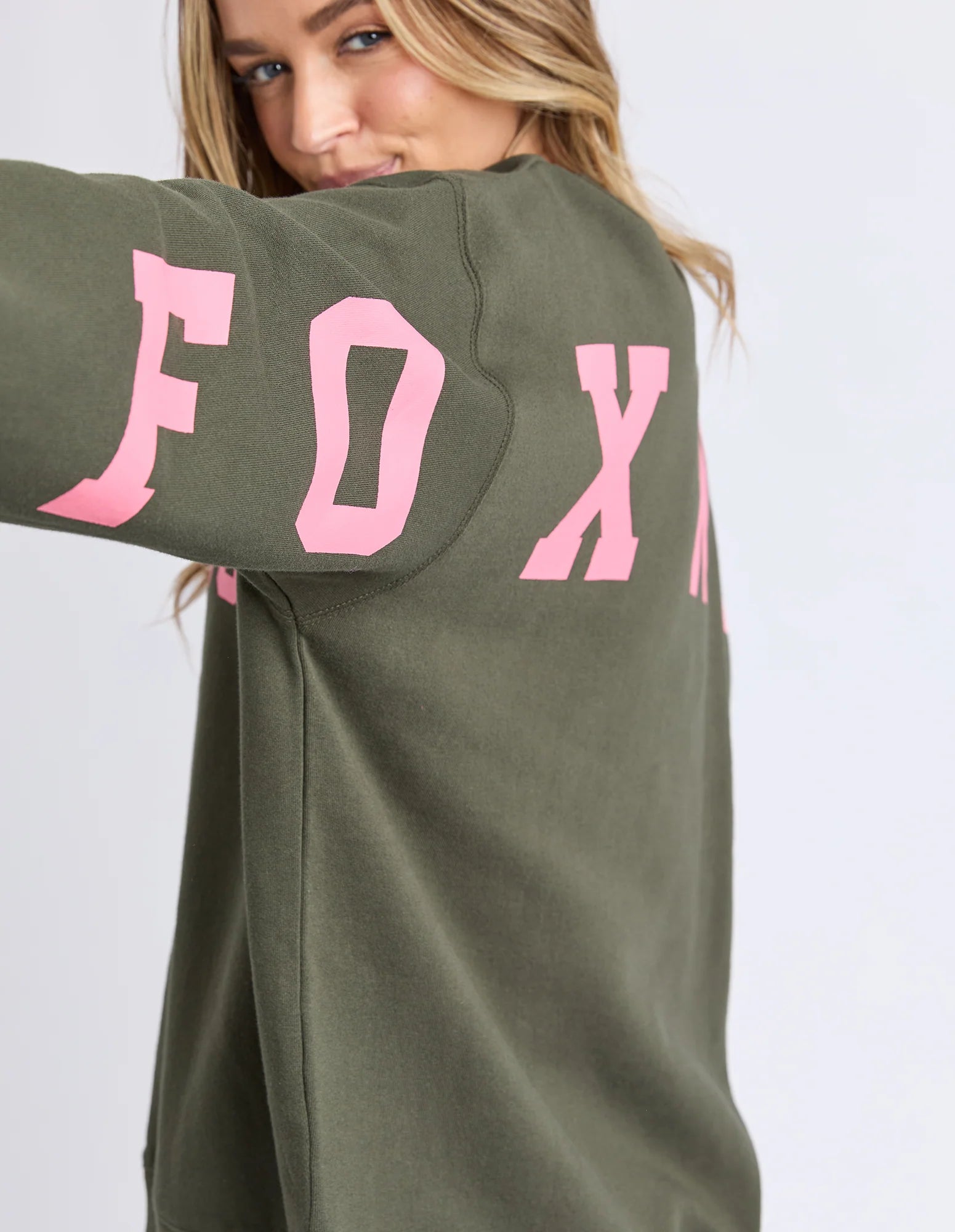 Image of Woman wearing a Foxwood green sweatshirt with pink text on a white background