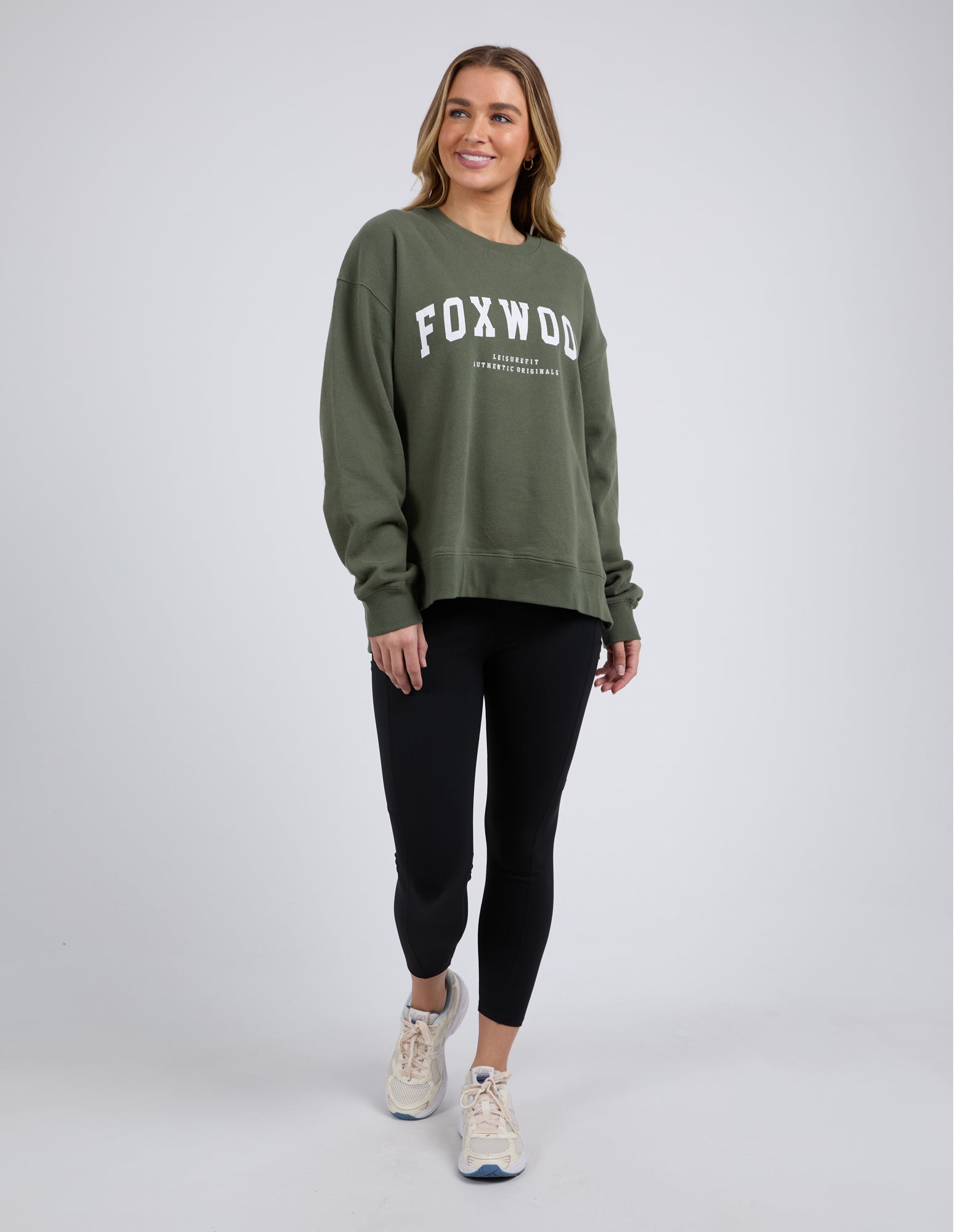 Woman wearing khaki Foxwood crew with black leggings on a white background