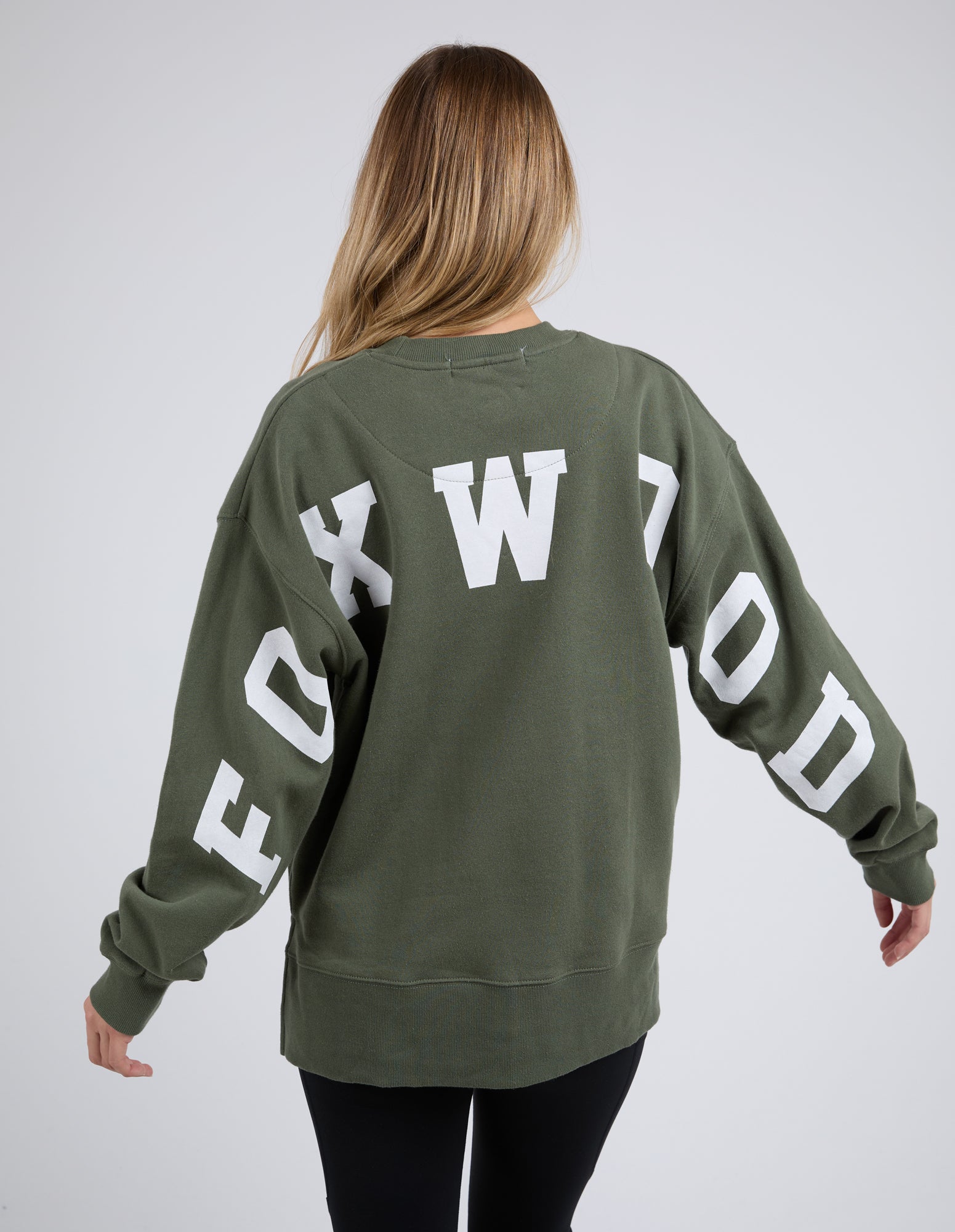 Woman wearing Foxwood khaki jumper with black leggings on a white background