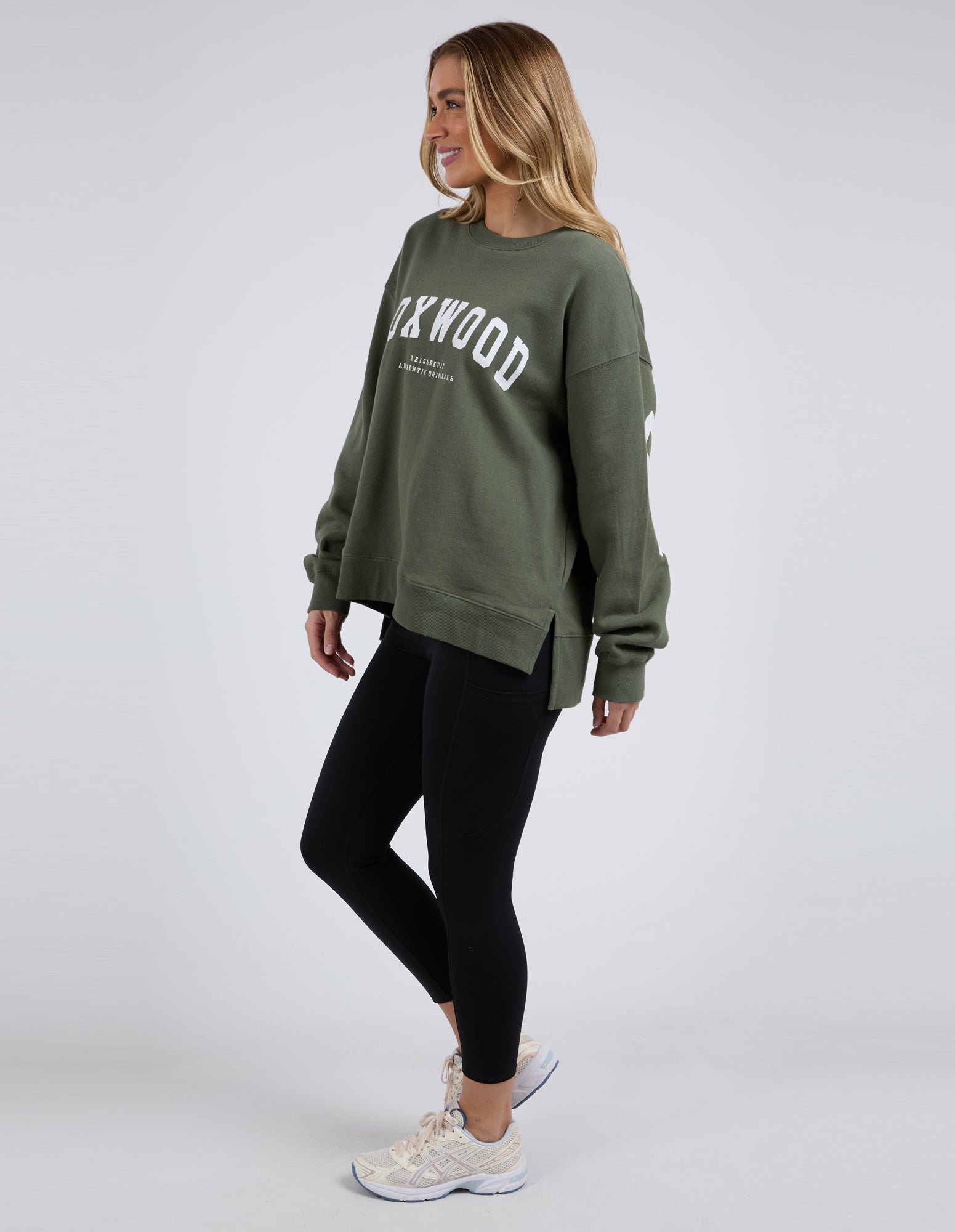 Woman wearing khaki Foxwood interval crew with black leggings on a white background