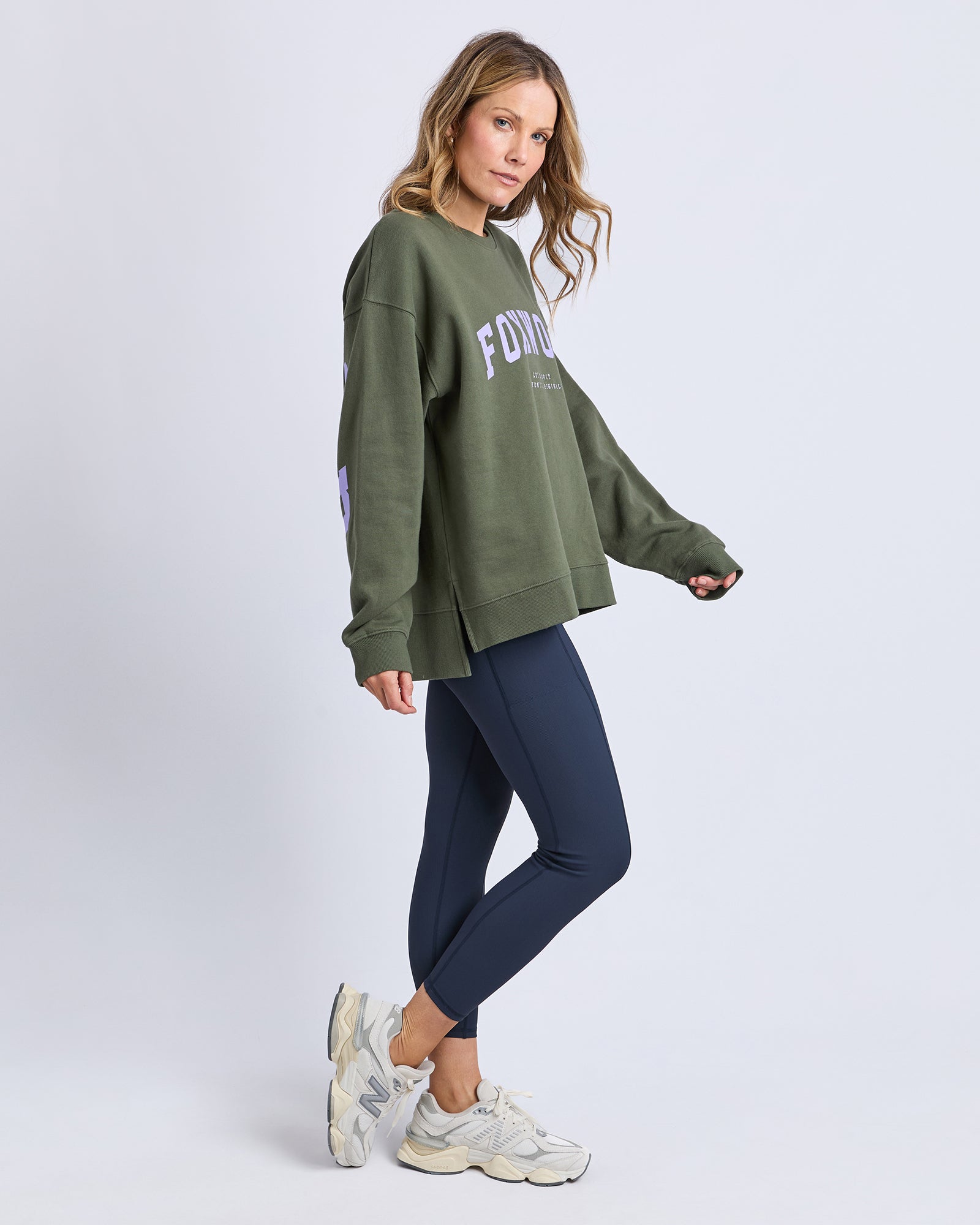 Woman wearing a green sweatshirt with text and dark blue leggings on a light gray background