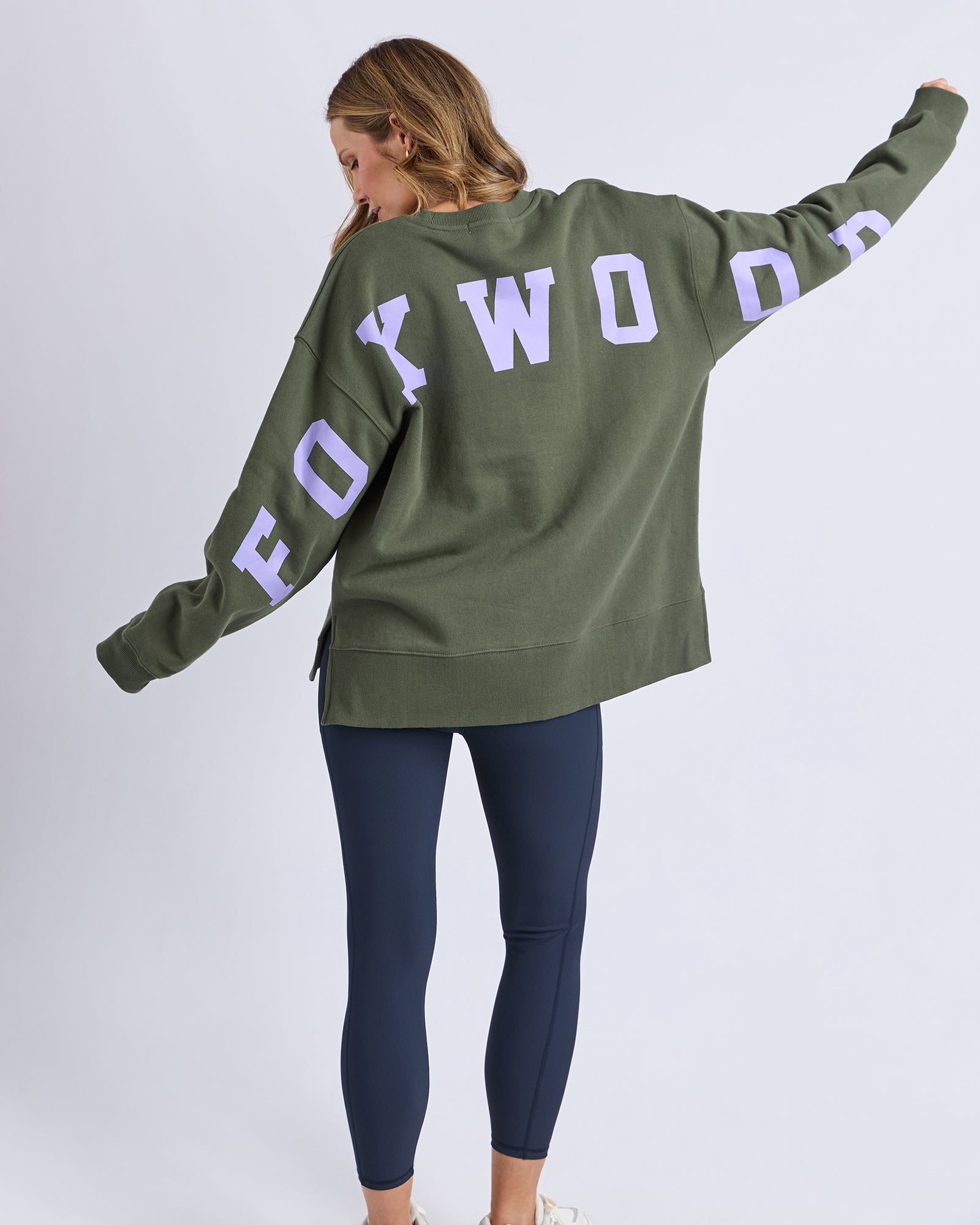 Image of Woman wearing a green sweatshirt with 'FOXWOOD' printed on the back against a white background