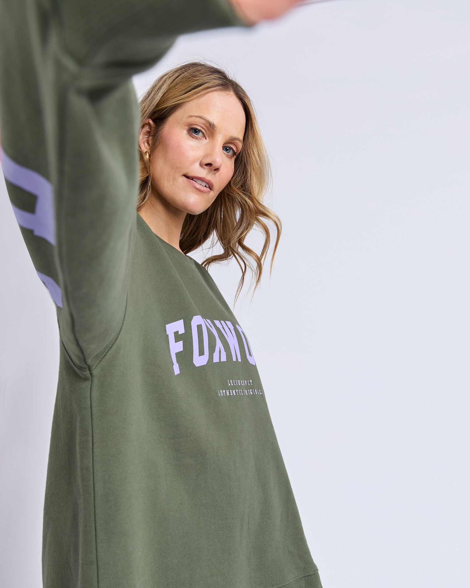 Image of Woman wearing a green sweatshirt with 'FOX' branding on a light gray background