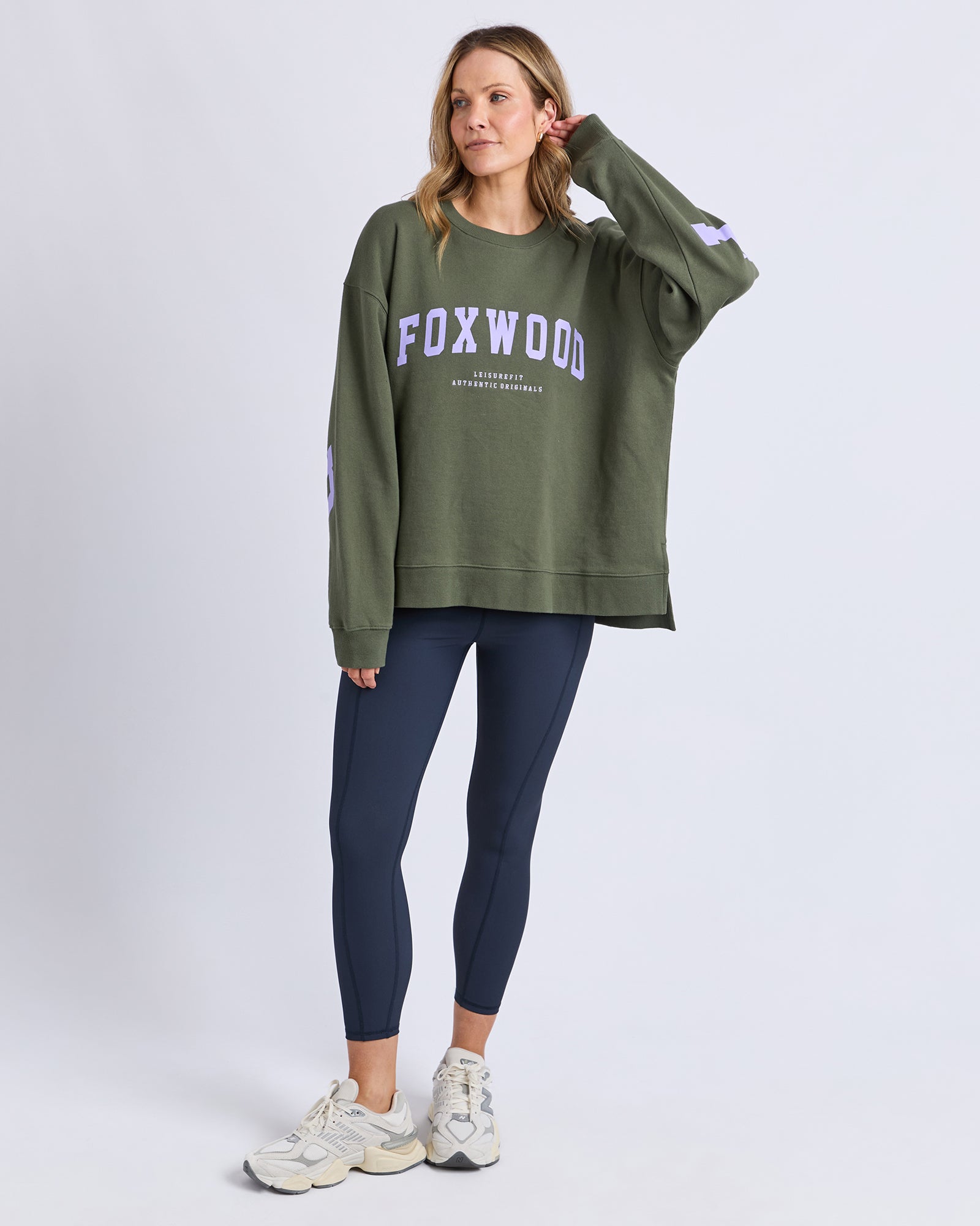 Image of Woman wearing a green 'FOXWOOD' sweatshirt and dark blue leggings on a white background