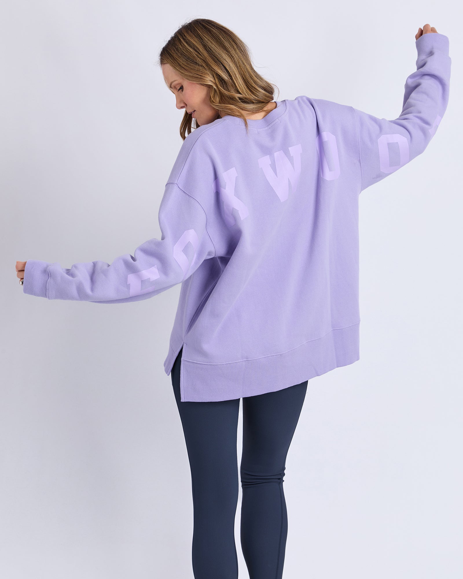 Woman wearing a light purple/lavender oversized jumper with 'Foxwood' branding on a white background