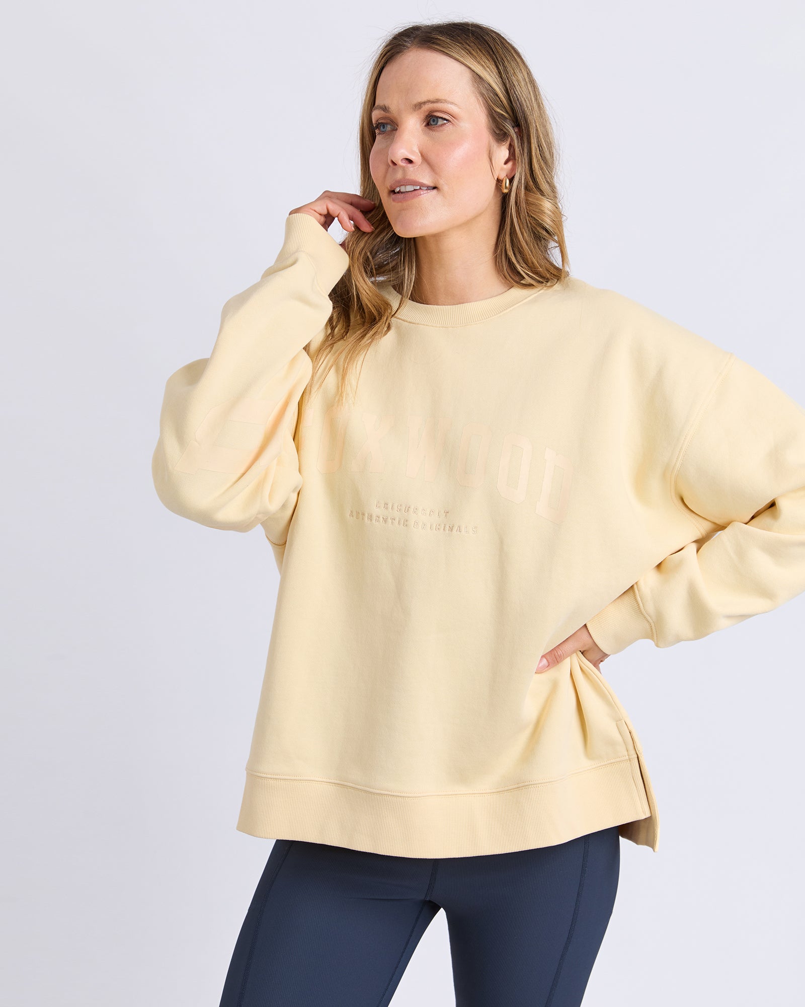 Woman wearing a light yellow lemon jumper and dark blue leggings on a plain background