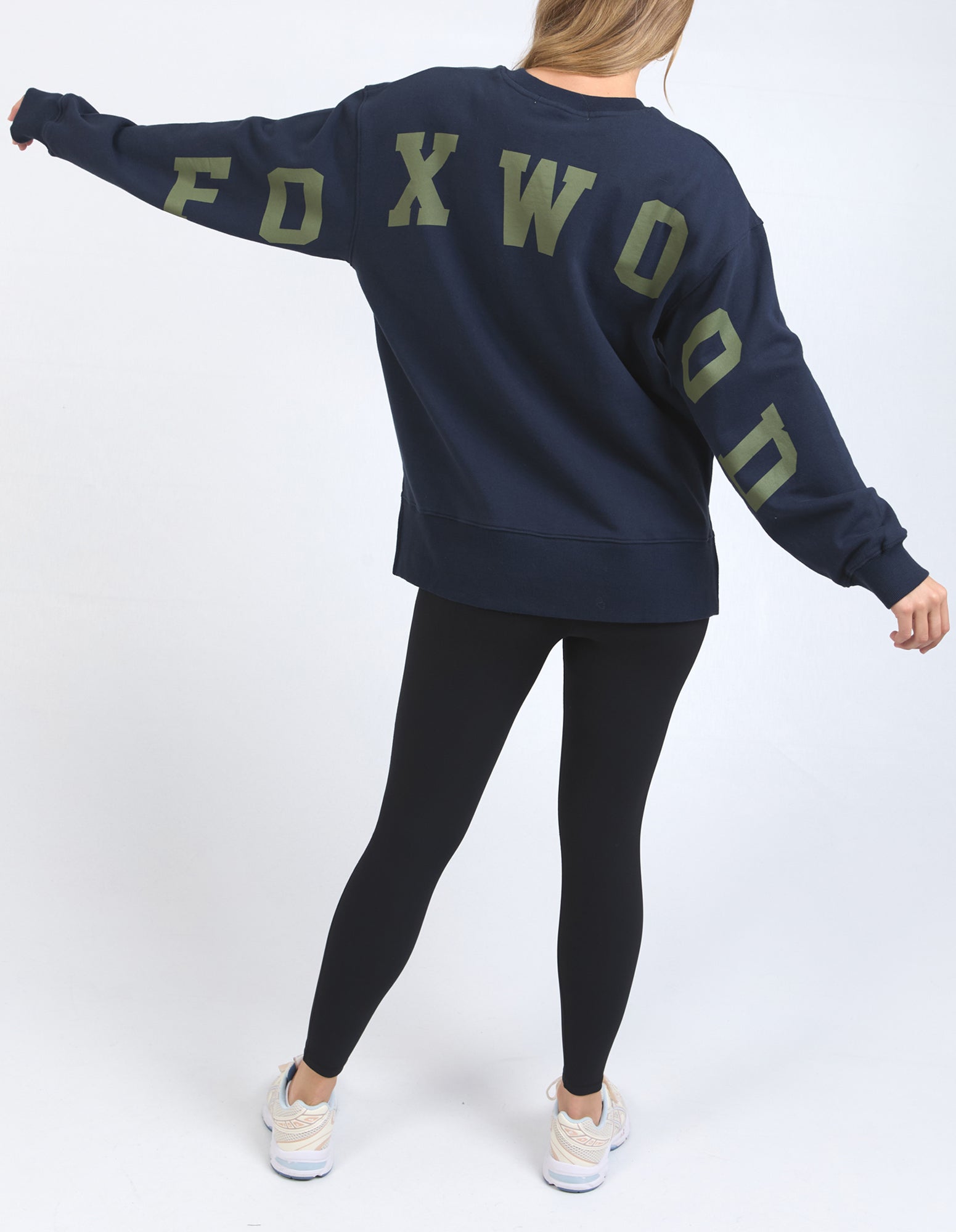 Image of Woman wearing a navy sweatshirt with 'FOXWOOD' printed on the back against a white background