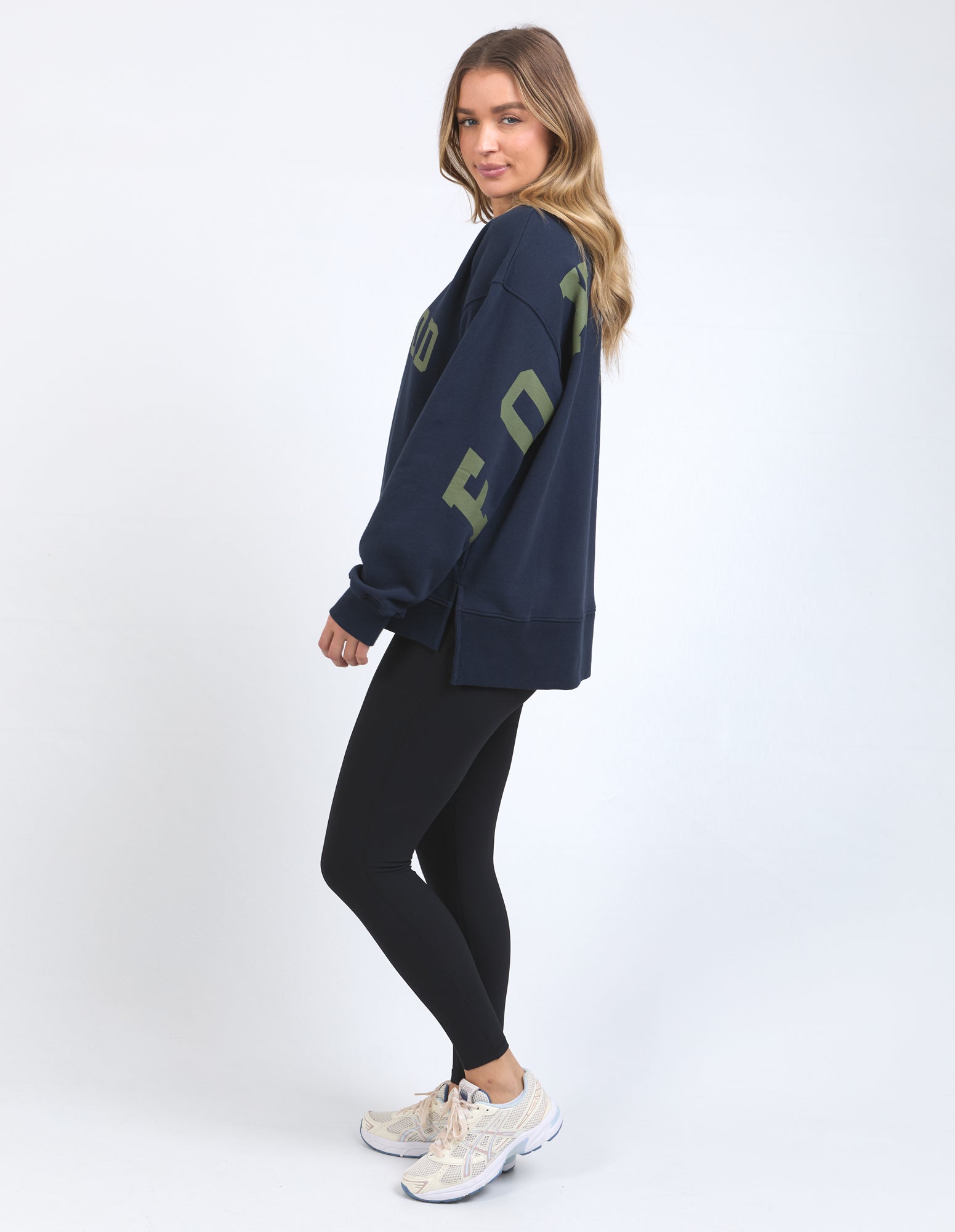Woman wearing a navy sweatshirt with green text and black leggings on a white background