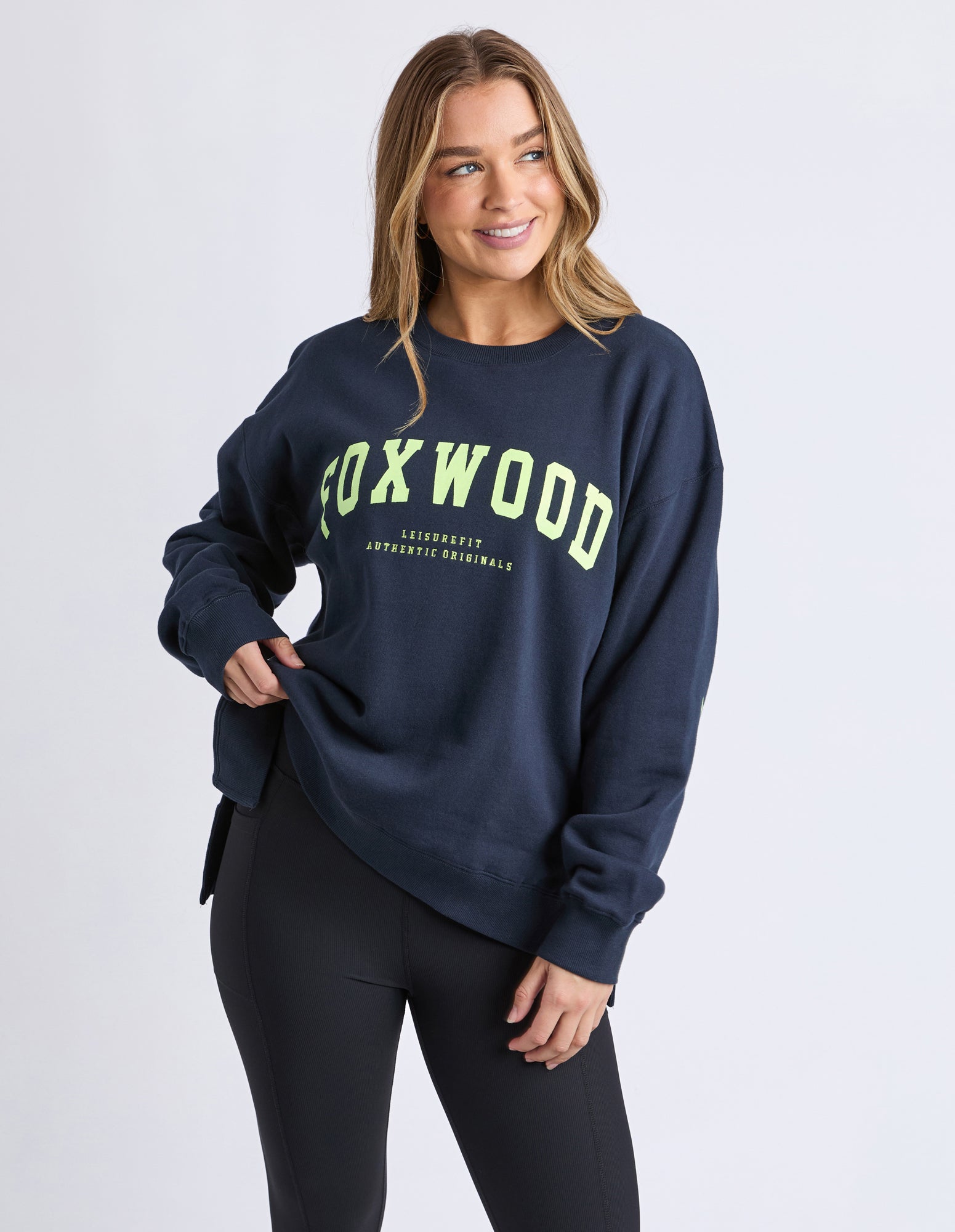 Image of Woman wearing a navy sweatshirt with 'FOXWOOD' printed on it against a white background