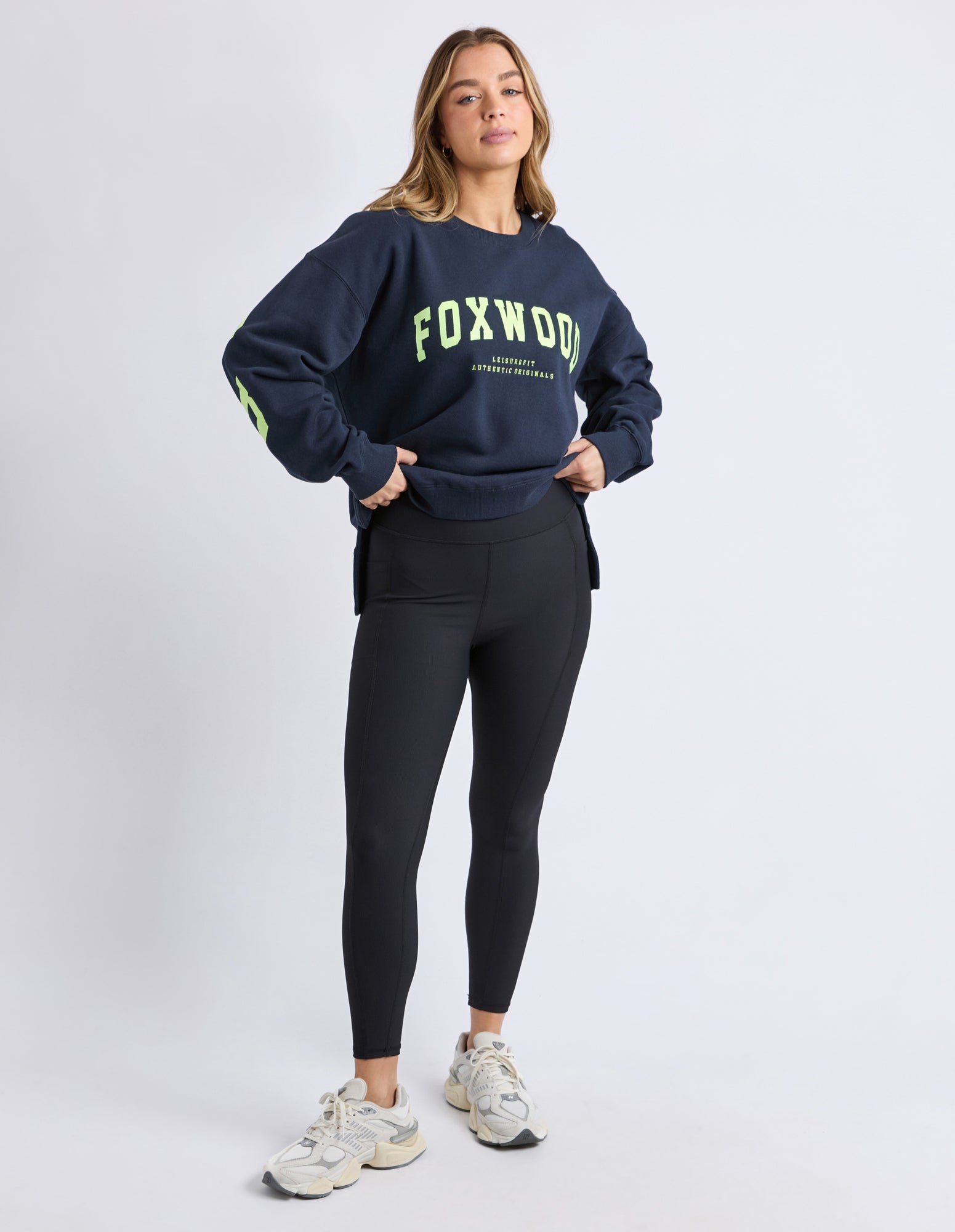 Image of Woman wearing a navy sweatshirt with 'FOXWOOD' branding and black leggings on a white background