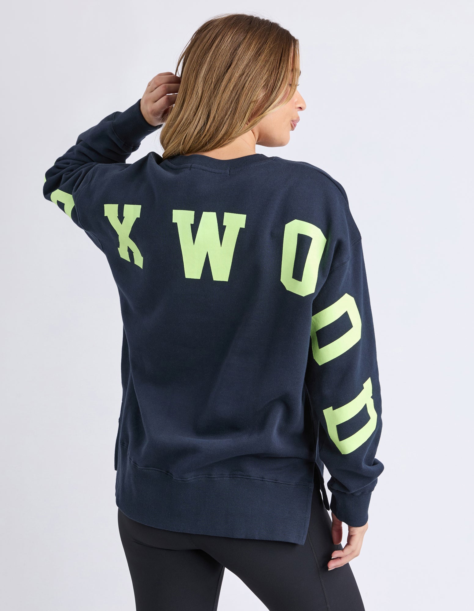 Woman wearing a navy sweatshirt with bright green letters on a plain background