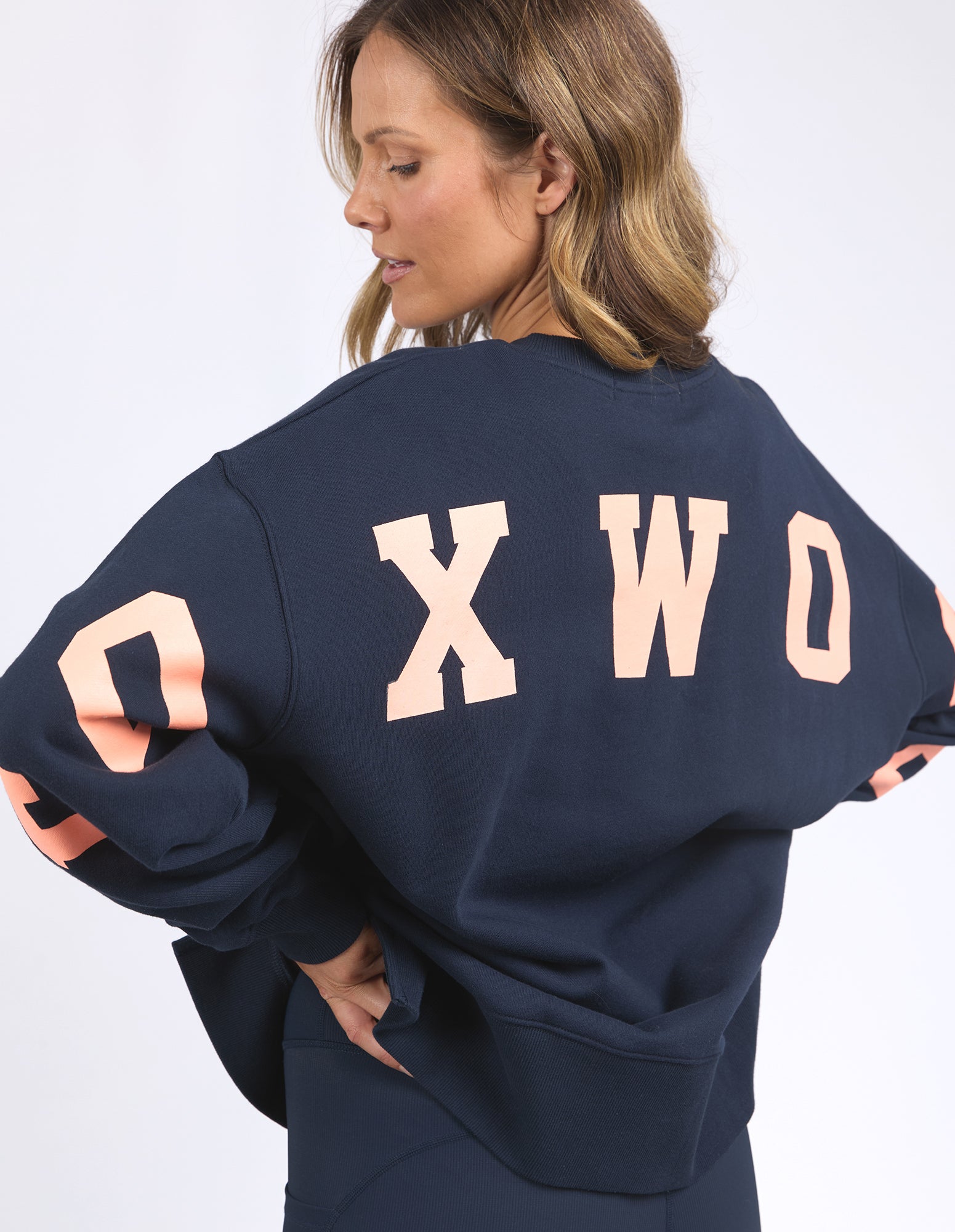 Image of Person wearing a navy blue sweatshirt with 'FOXWOOD' printed on the back against a white background