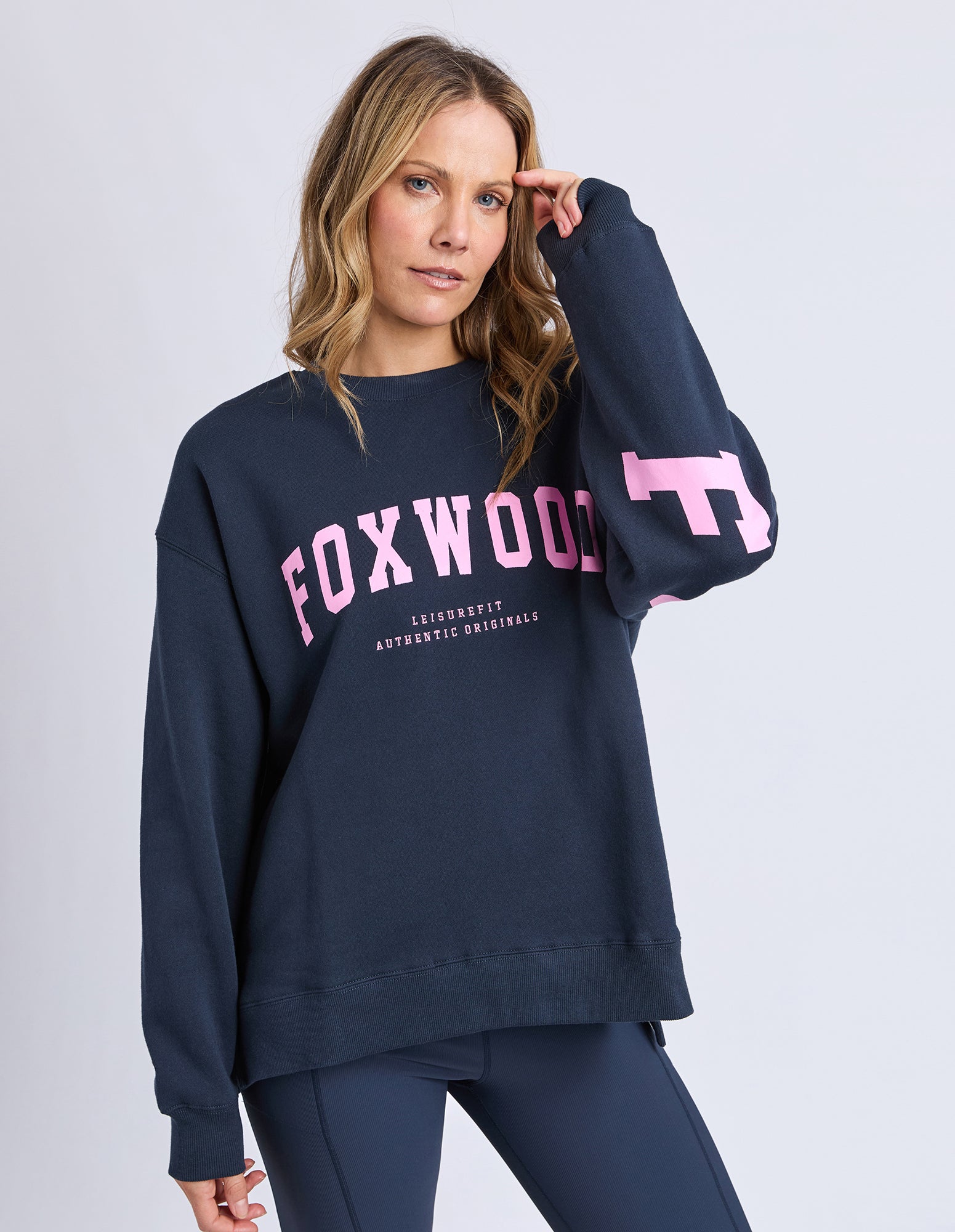 Image of Woman wearing a navy sweatshirt with pink text and logo on a light gray background