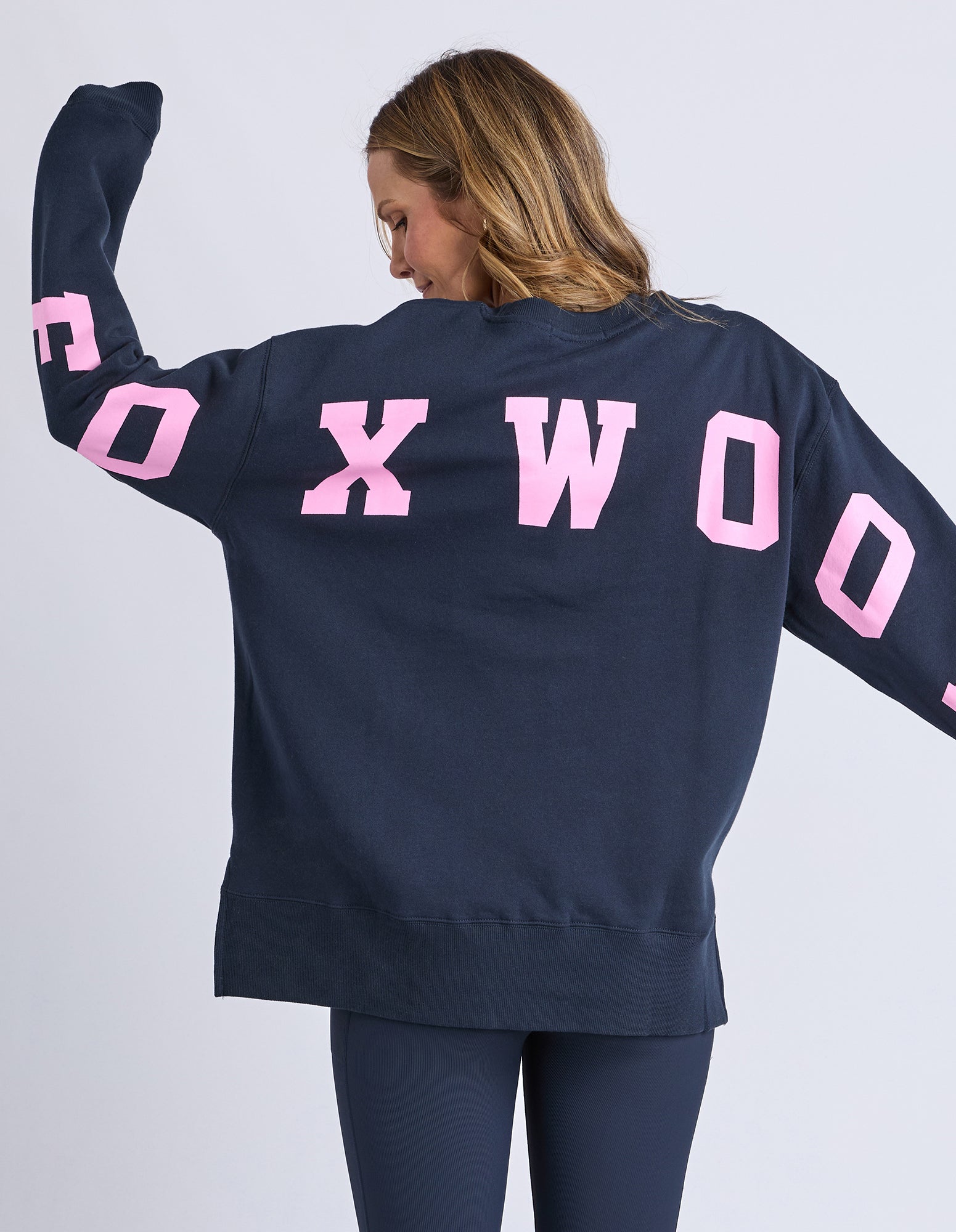 Image of Woman wearing a navy sweatshirt with pink text on a white background