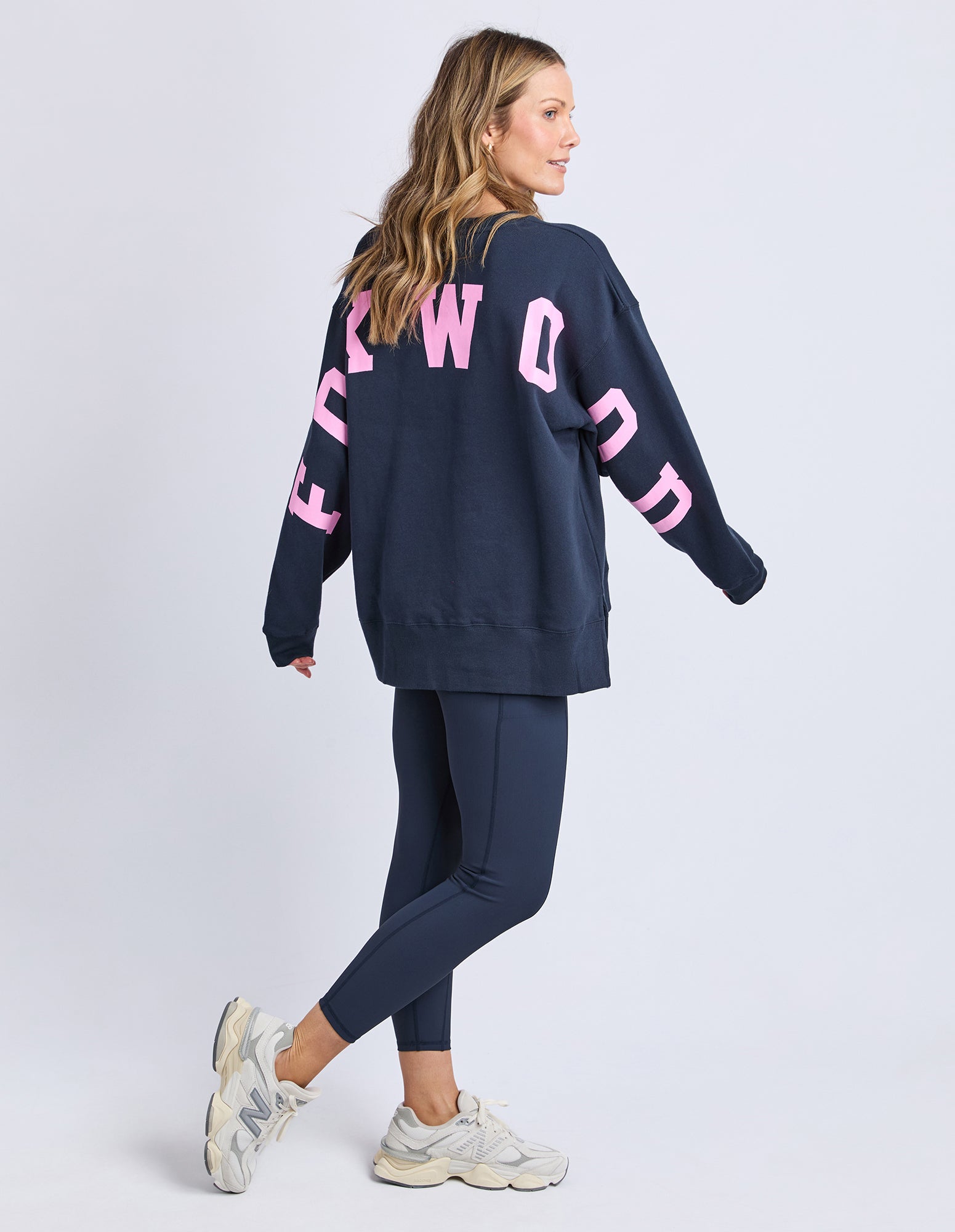 Woman wearing a navy sweatshirt with pink text and matching pants on a light gray background