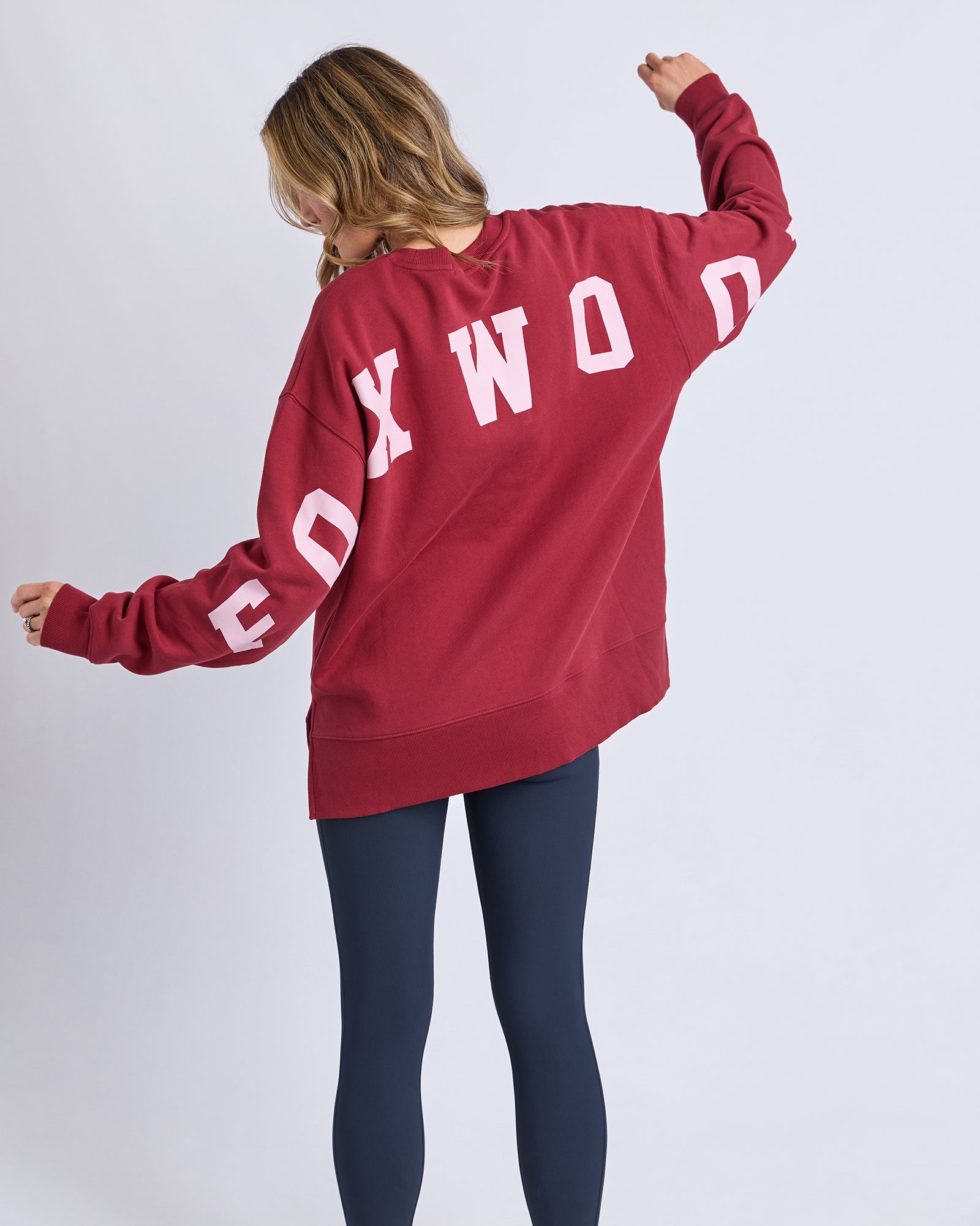 Image of Woman wearing a red sweatshirt with 'FOXWOOD' printed on the back, standing against a white background.