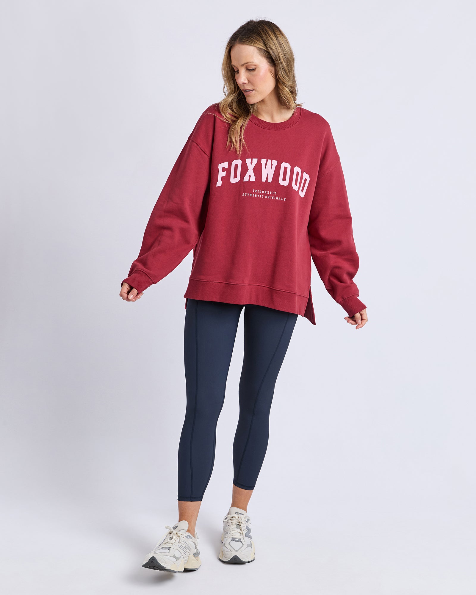 Woman wearing a red 'FOXWOOD' sweatshirt and dark blue leggings on a light gray background
