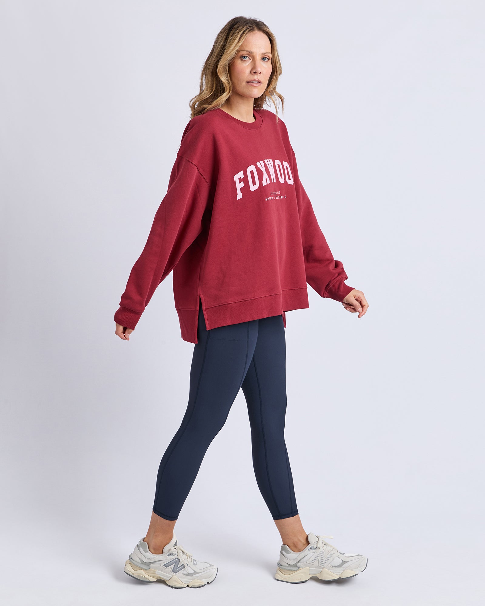 Image of Woman wearing a red 'FOXWOOD' sweatshirt and navy leggings on a white background