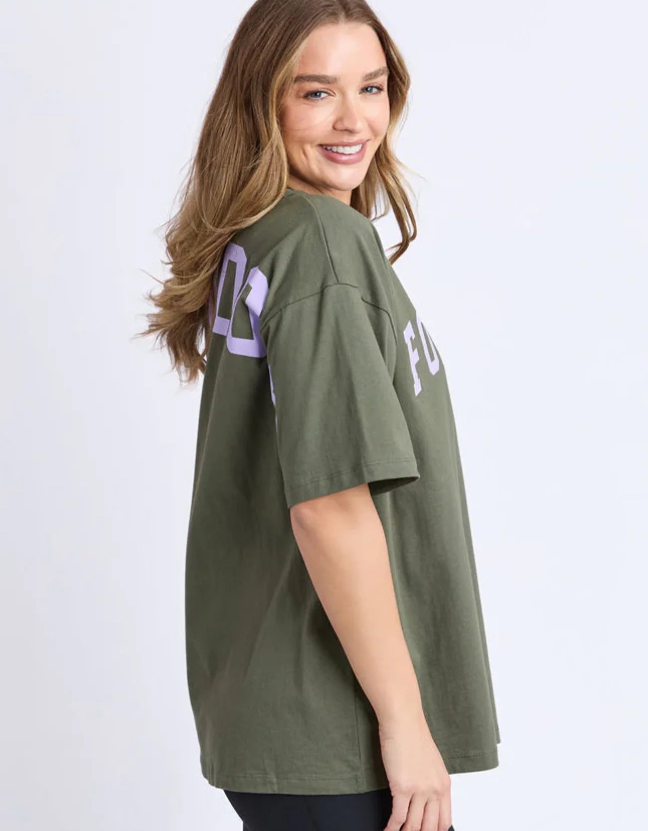 Image of Woman wearing a Foxwood green oversized t-shirt with text on a white background