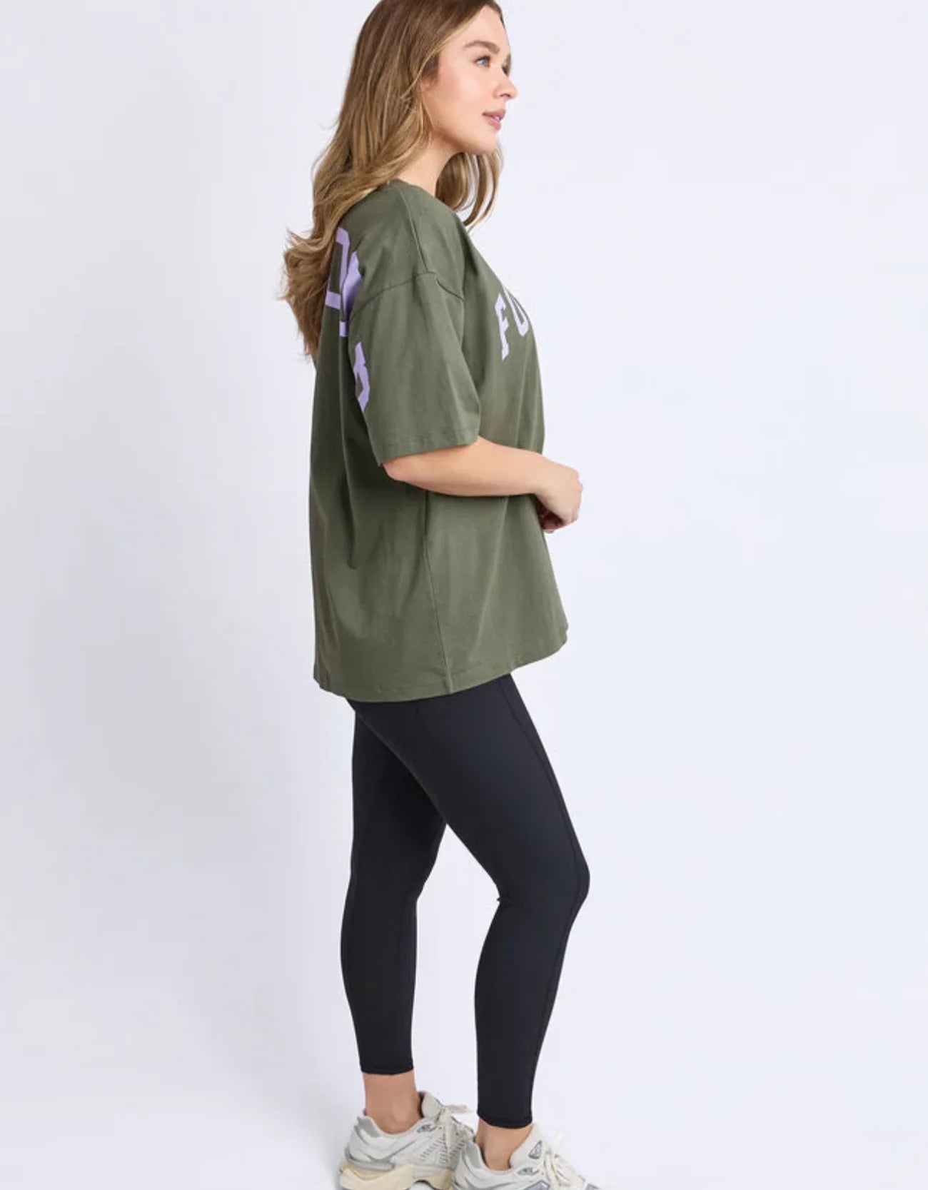 Woman wearing a Foxwood green oversized t-shirt and black leggings on a white background
