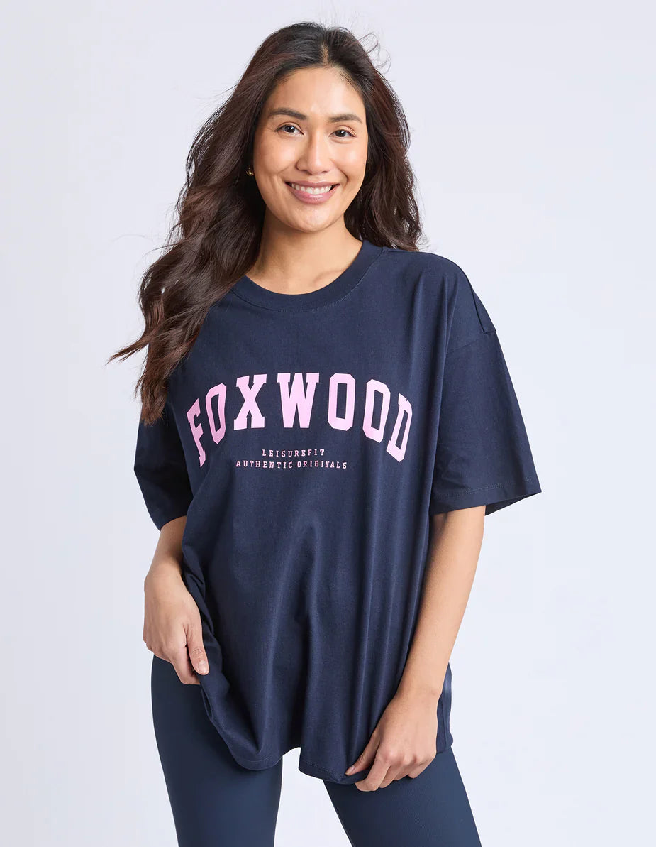 Image of Woman wearing a navy blue t-shirt with 'FOXWOOD' printed in pink on a white background