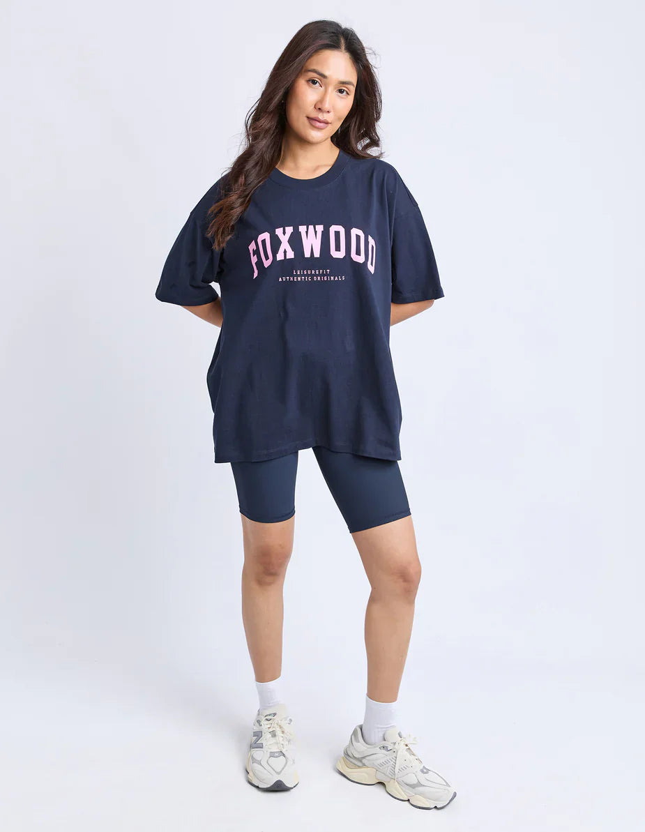 Image of Woman wearing a navy 'FOXWOOD' t-shirt and shorts on a white background