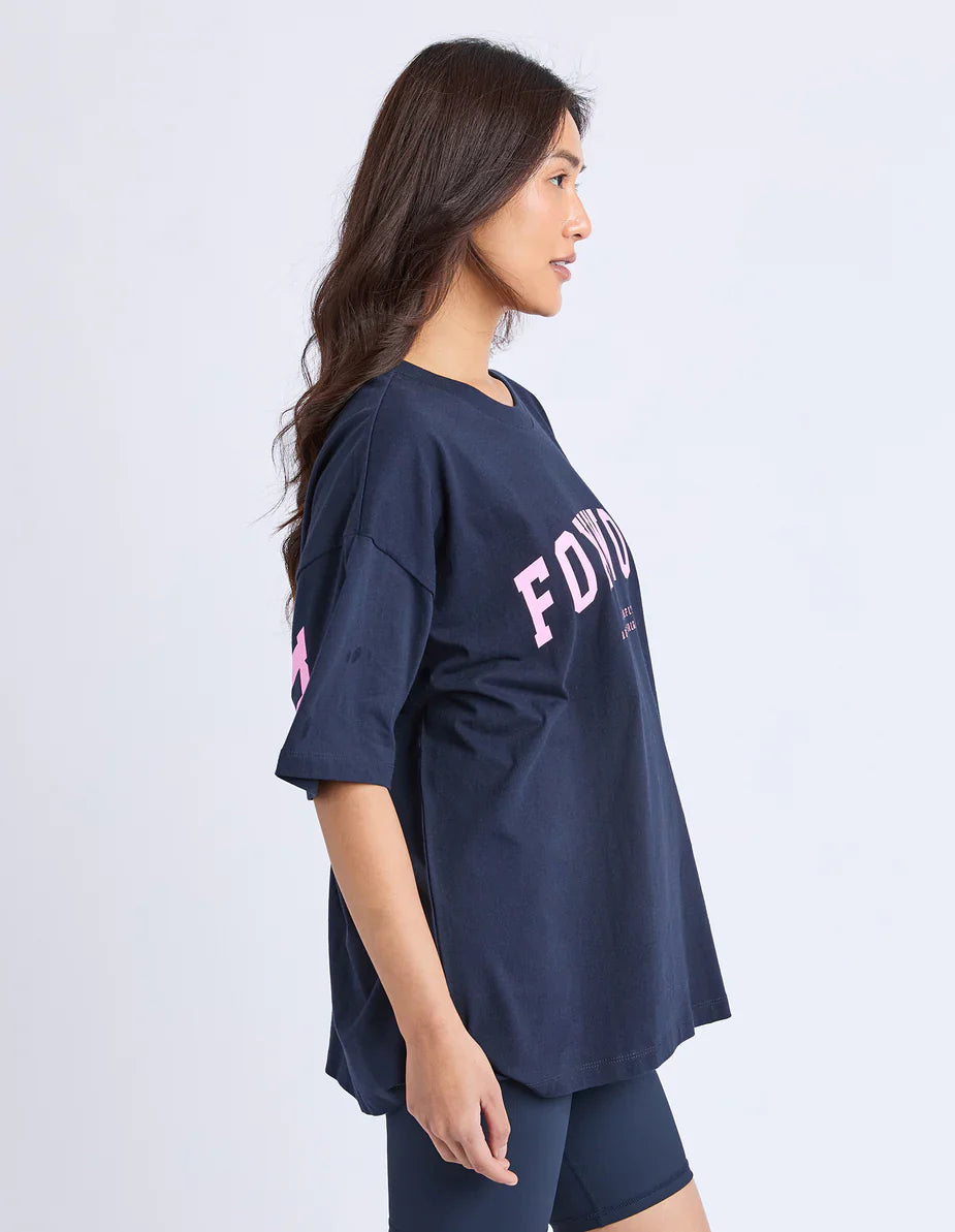 Woman wearing a Foxwood navy blue oversized t-shirt with pink text on a white background