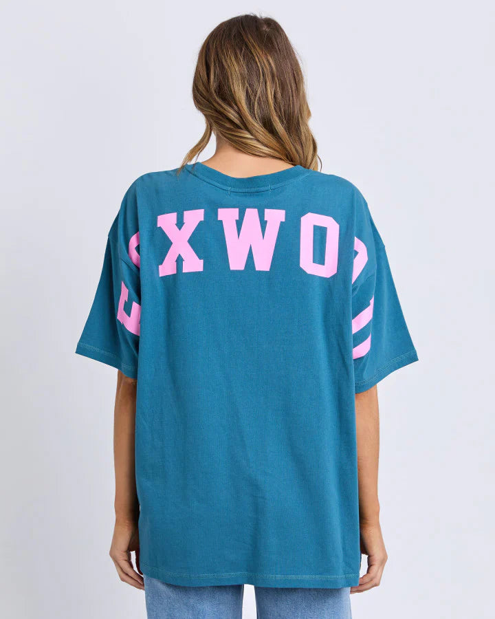 Image of Woman wearing a Foxwood teal t-shirt with pink text on the back against a white background