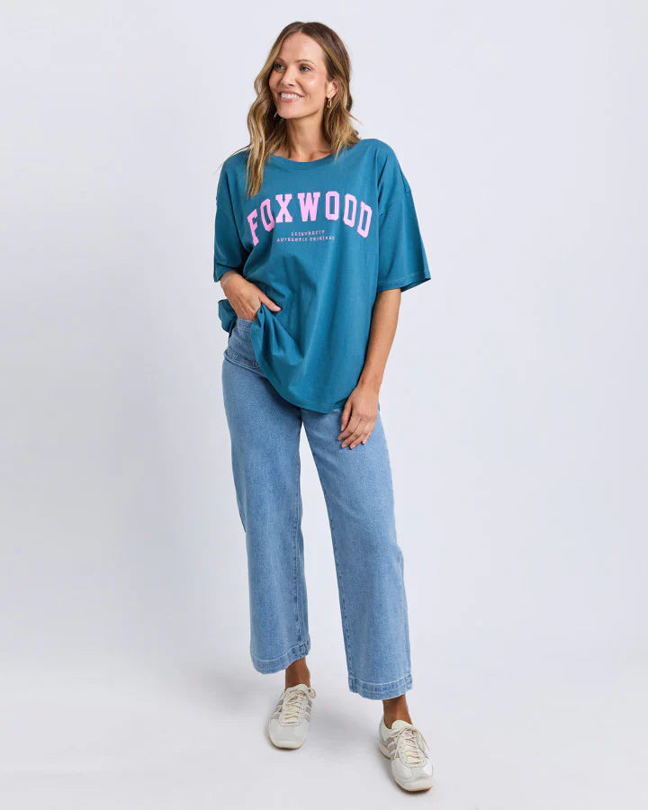 Woman wearing a Foxwood teal t-shirt with 'Foxwood' printed on it, standing against a white background