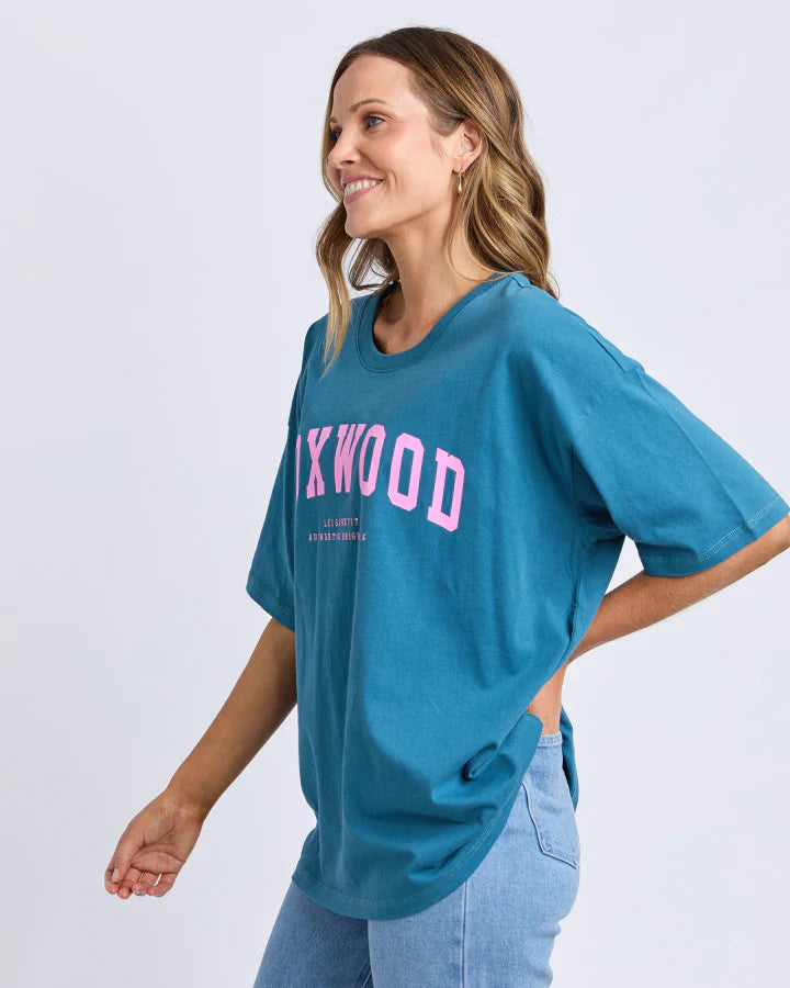 Woman wearing a Foxwood teal t-shirt with 'FOXWOOD' printed in pink on a white background