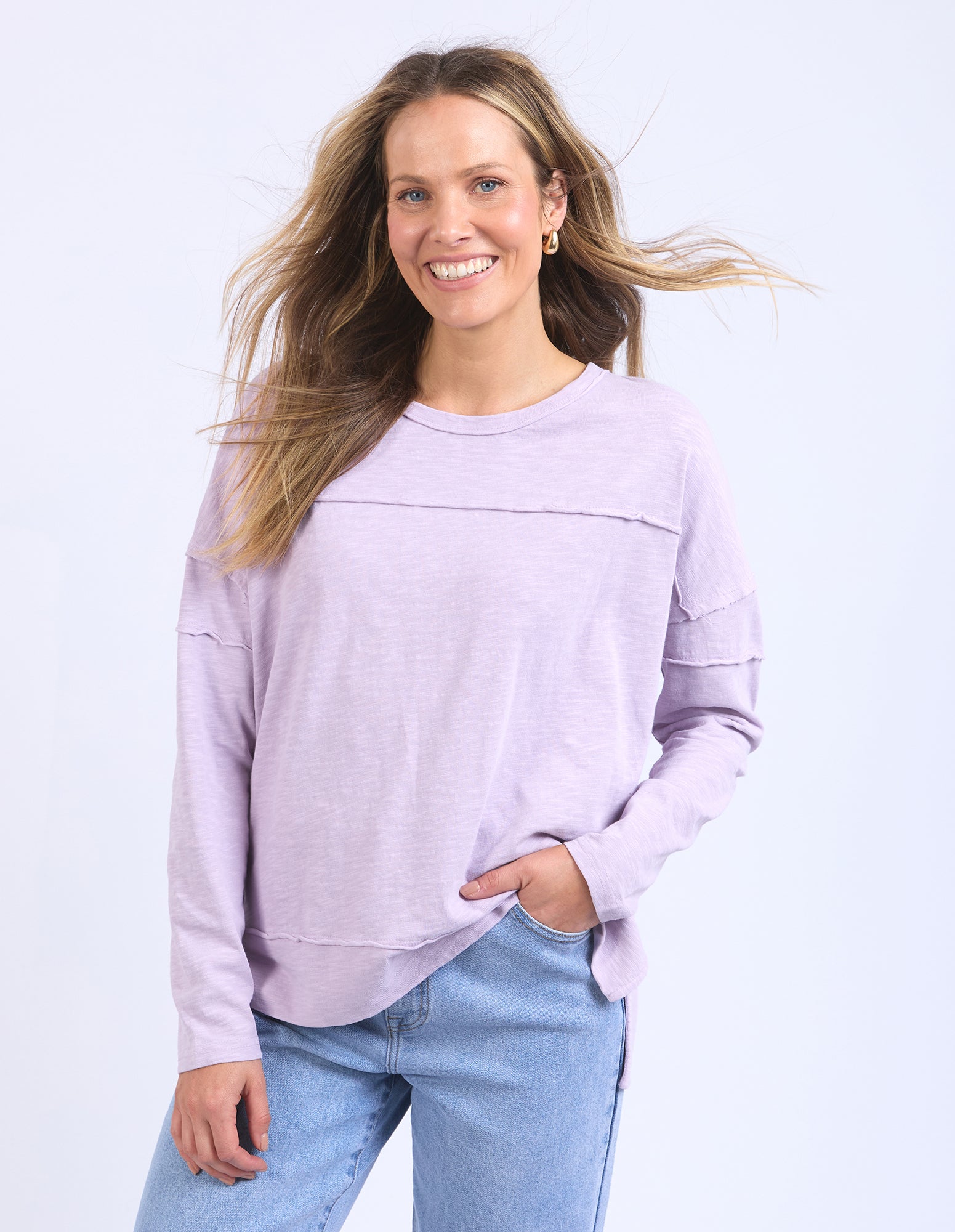 Image of Woman wearing a light purple lavender long sleeve tee and blue jeans against a white background
