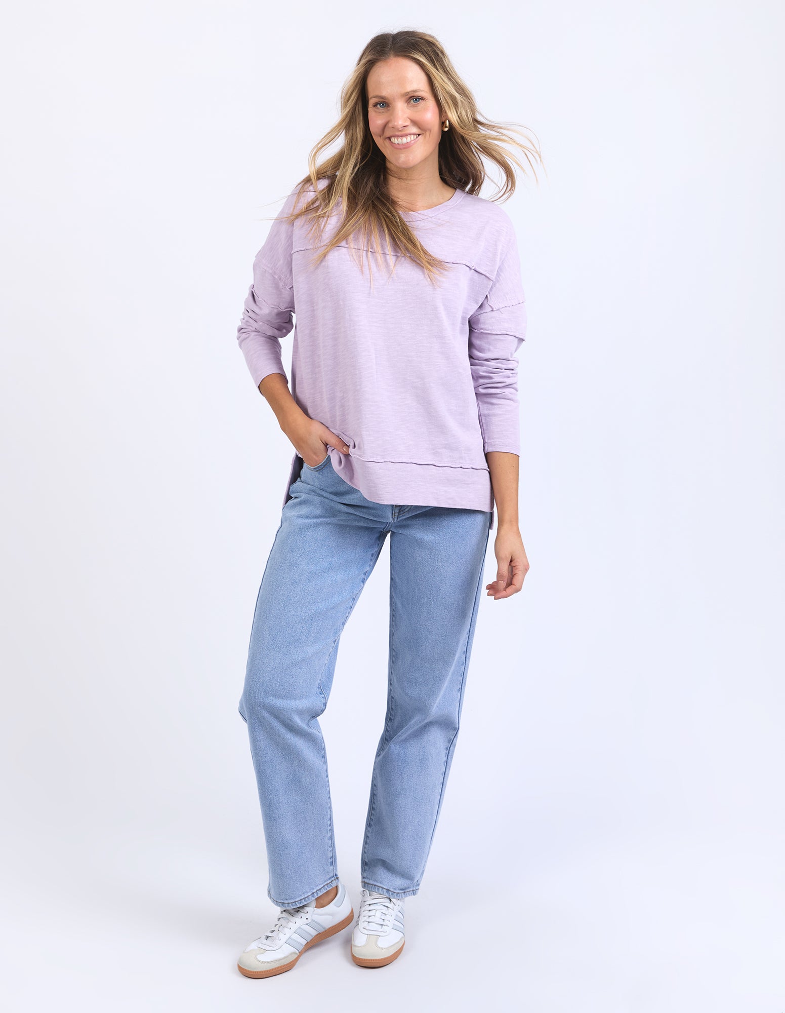 Image of Woman wearing a light purple lavender long sleeve top and blue jeans on a white background
