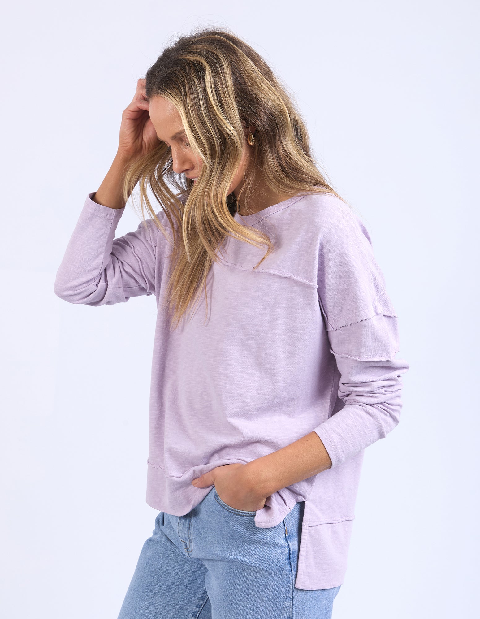Image of Woman wearing a light purple lavender long sleeve tee and blue jeans on a white background