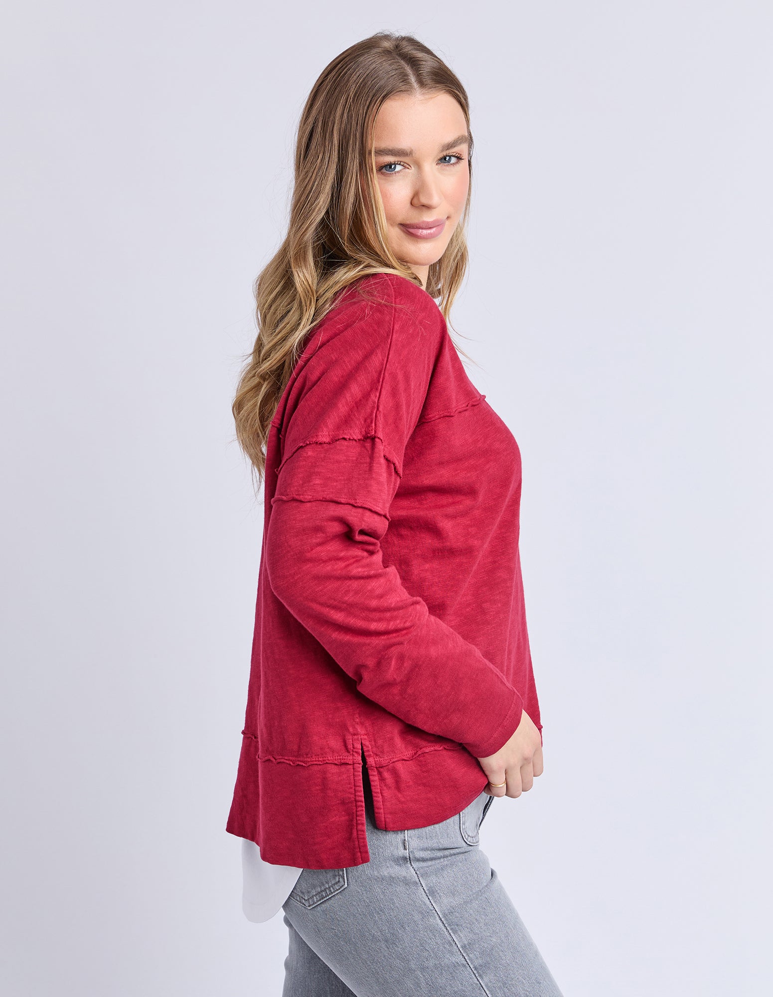 Image of Side view of a Woman wearing a Foxwood red long sleeve tee on a light grey background