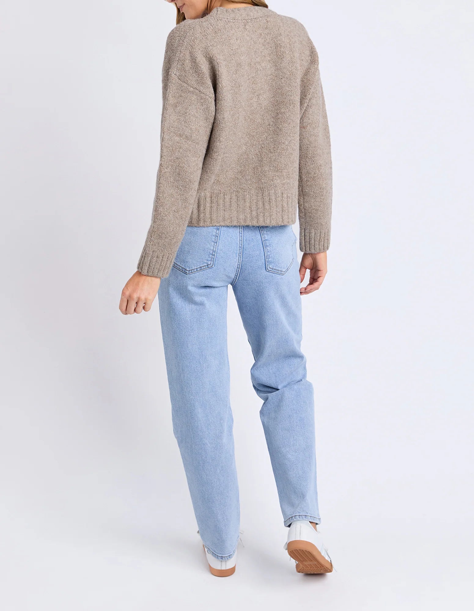 Image of Woman wearing a Foxwood beige sweater and light blue jeans on a white background