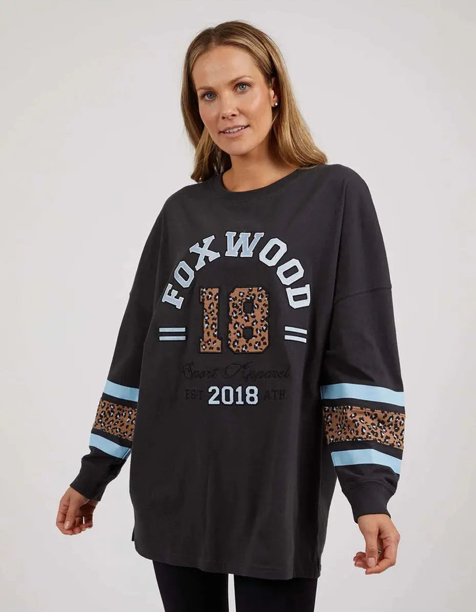 Image of A woman wearing a black Foxwood long-sleeve graphic sweatshirt with leopard print and light blue stripe details on the sleeves, set against a plain light gray background.