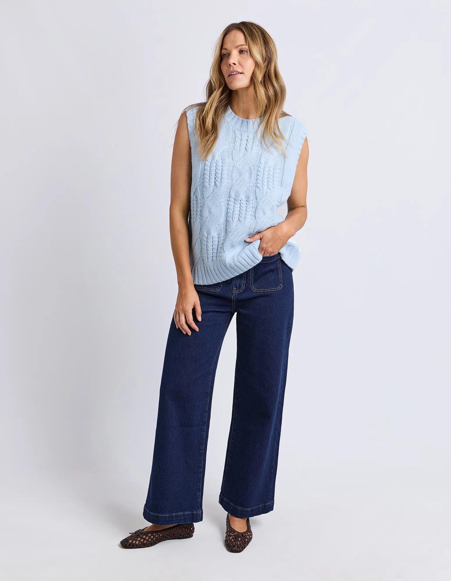 Woman wearing a Foxwood light blue sleeveless top and dark blue jeans on a white background