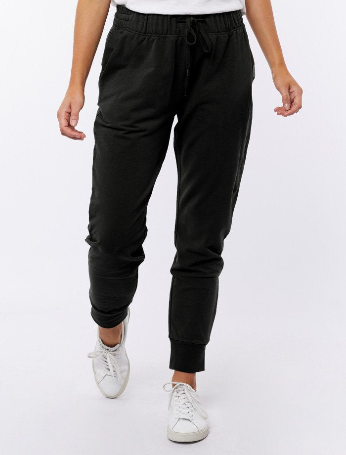 Image of Woman wearing Foxwood black lazy day tracksuit pants with a white singlet on a white background