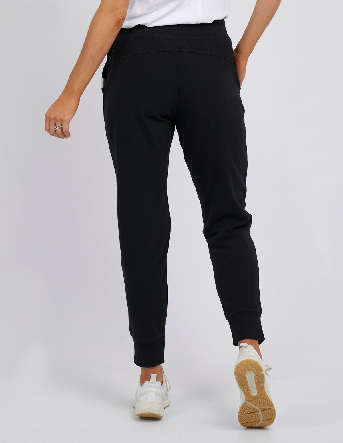 Woman wearing Foxwood black lazy day tracksuit pants with a white singlet on a white background